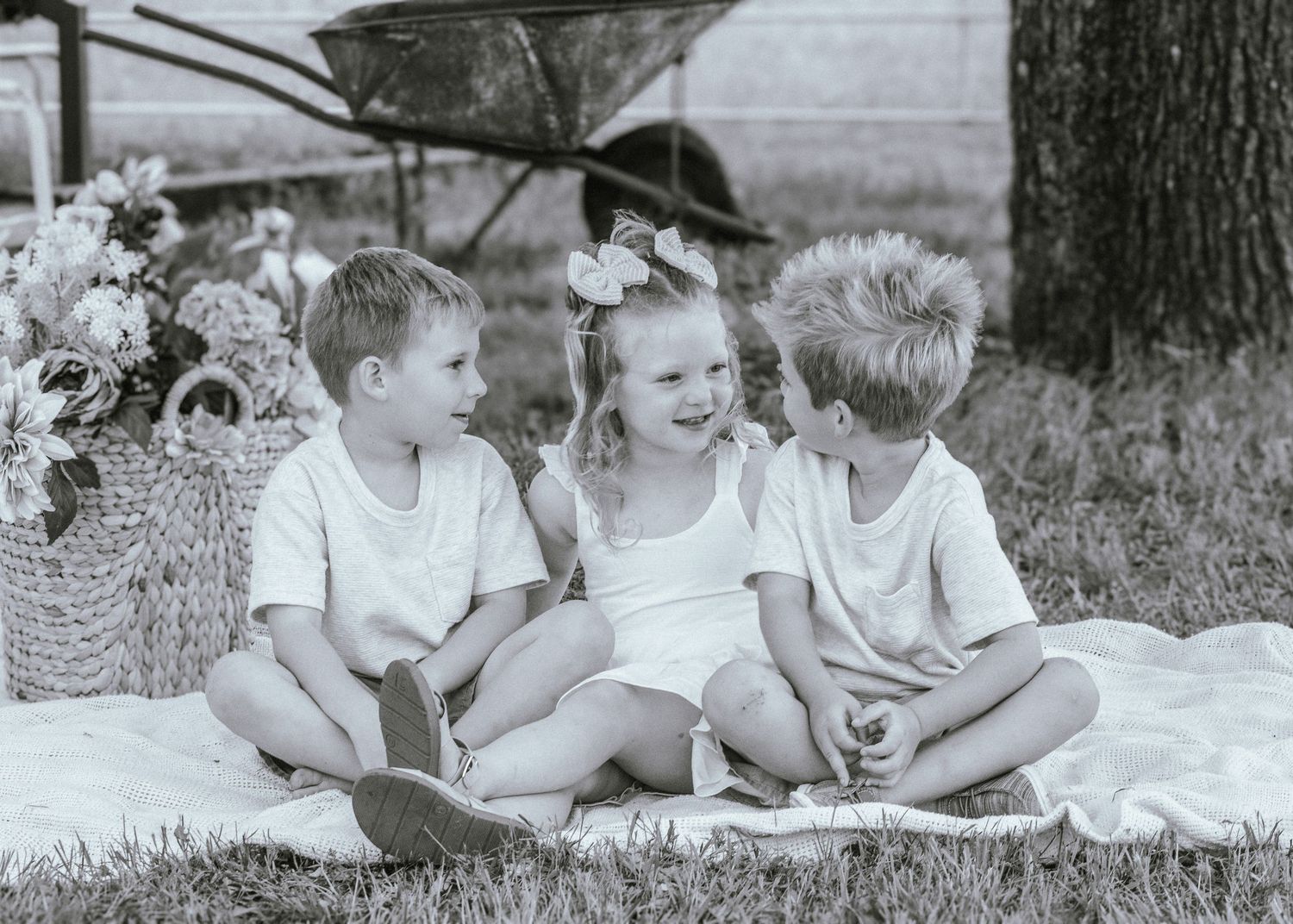 A vintage black and white series of children laying in the grass under a tree.