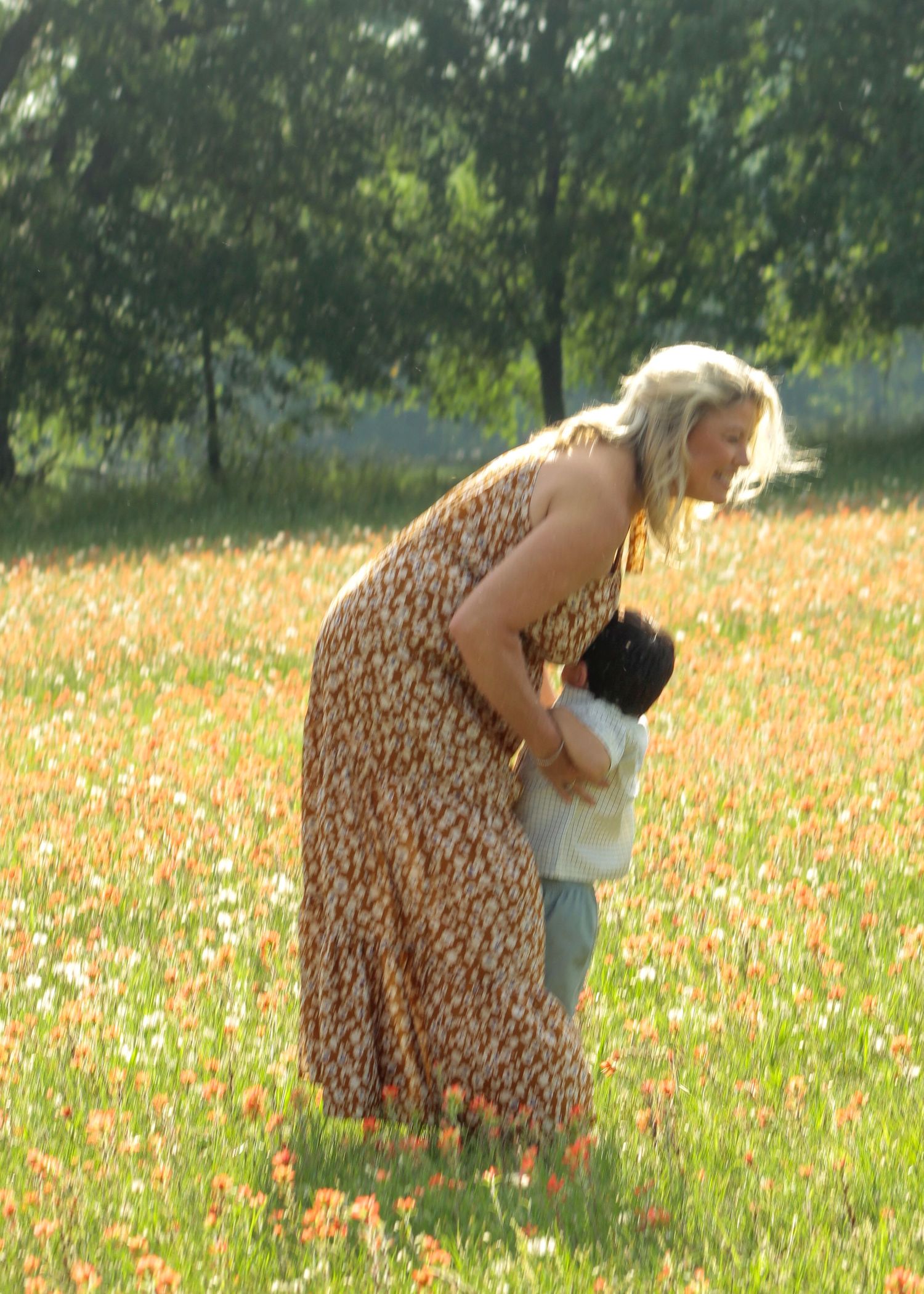 Woman in floral dress bending down to interact with a small child in a vibrant wildflower field.