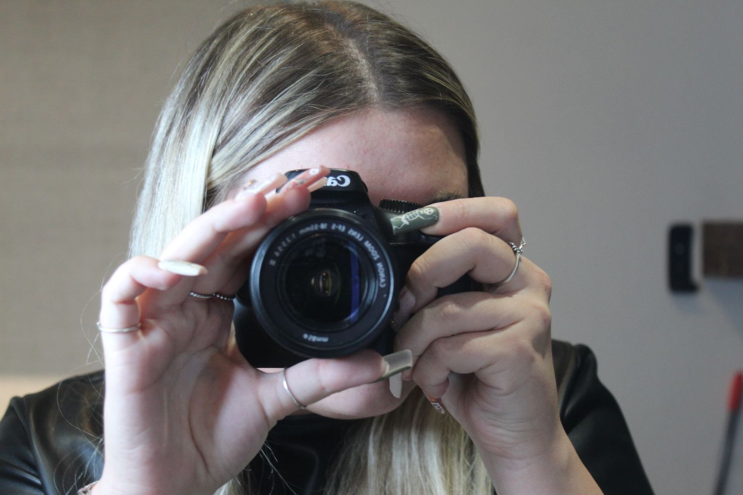 Someone taking a self portrait photo with a DSLR camera against a light colored wall.