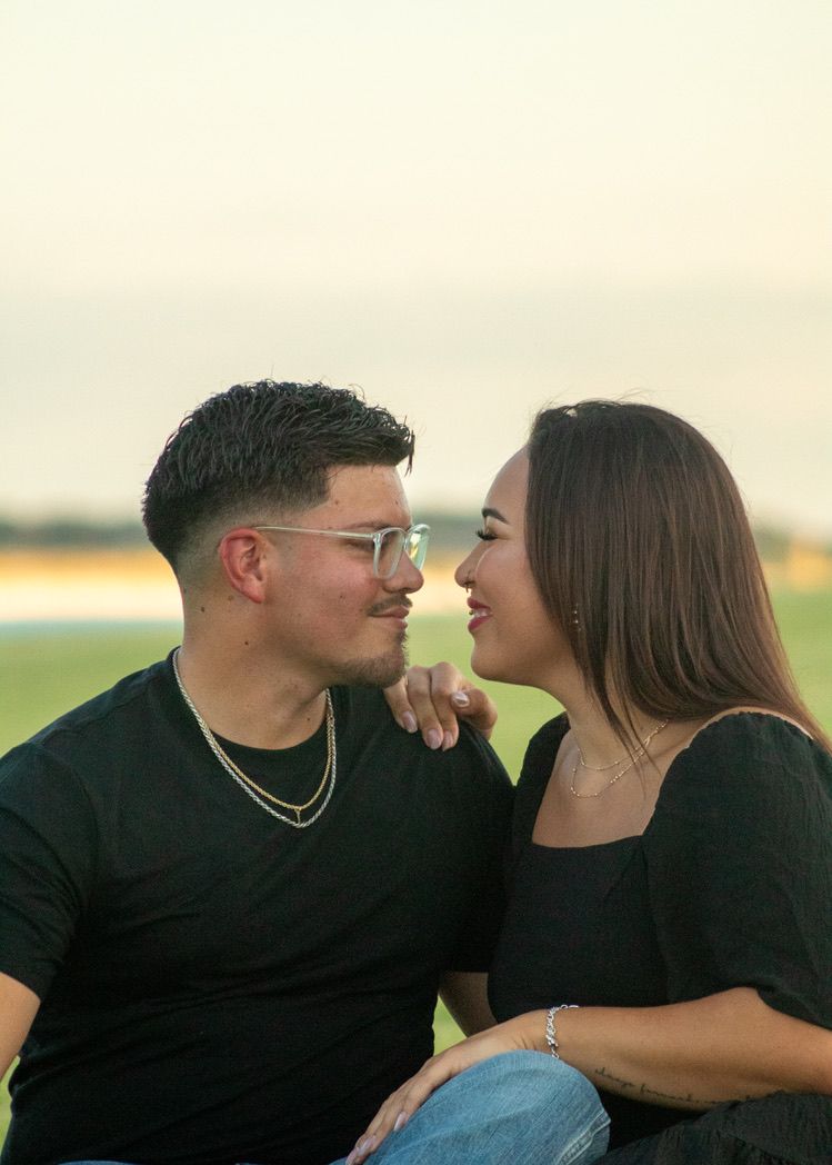 A couple in black outfits share an intimate moment outdoors at sunset in a romantic setting.