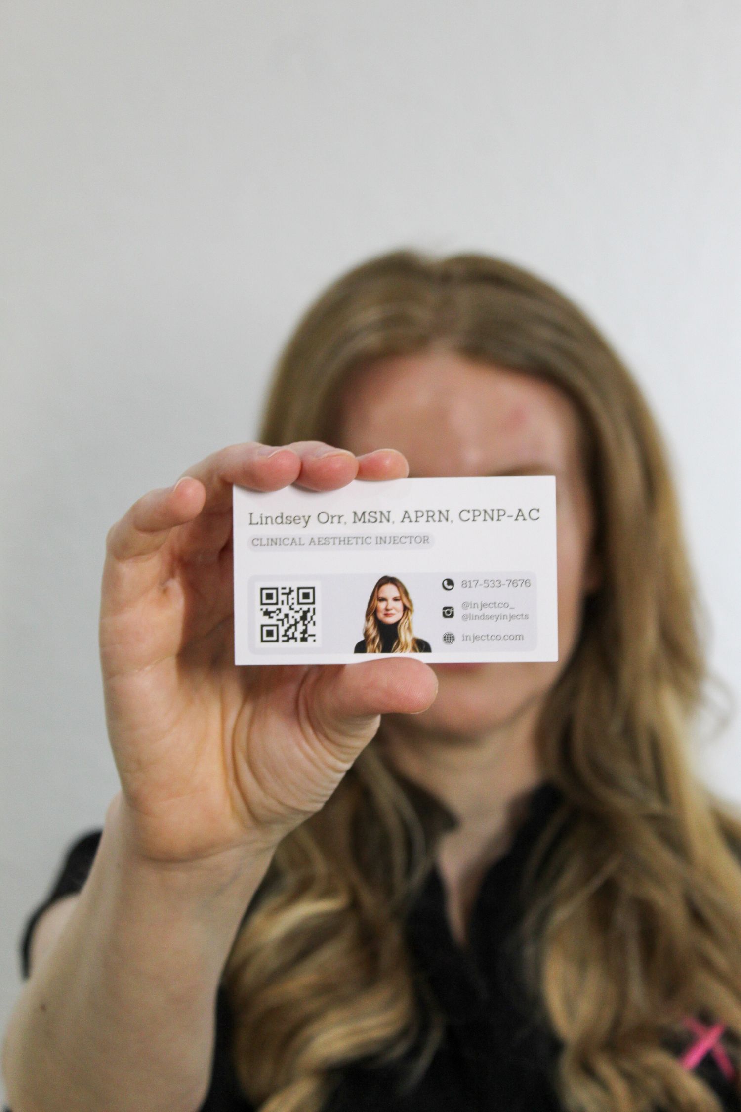 Professional holds up a white business card displaying contact information against a light colored background.