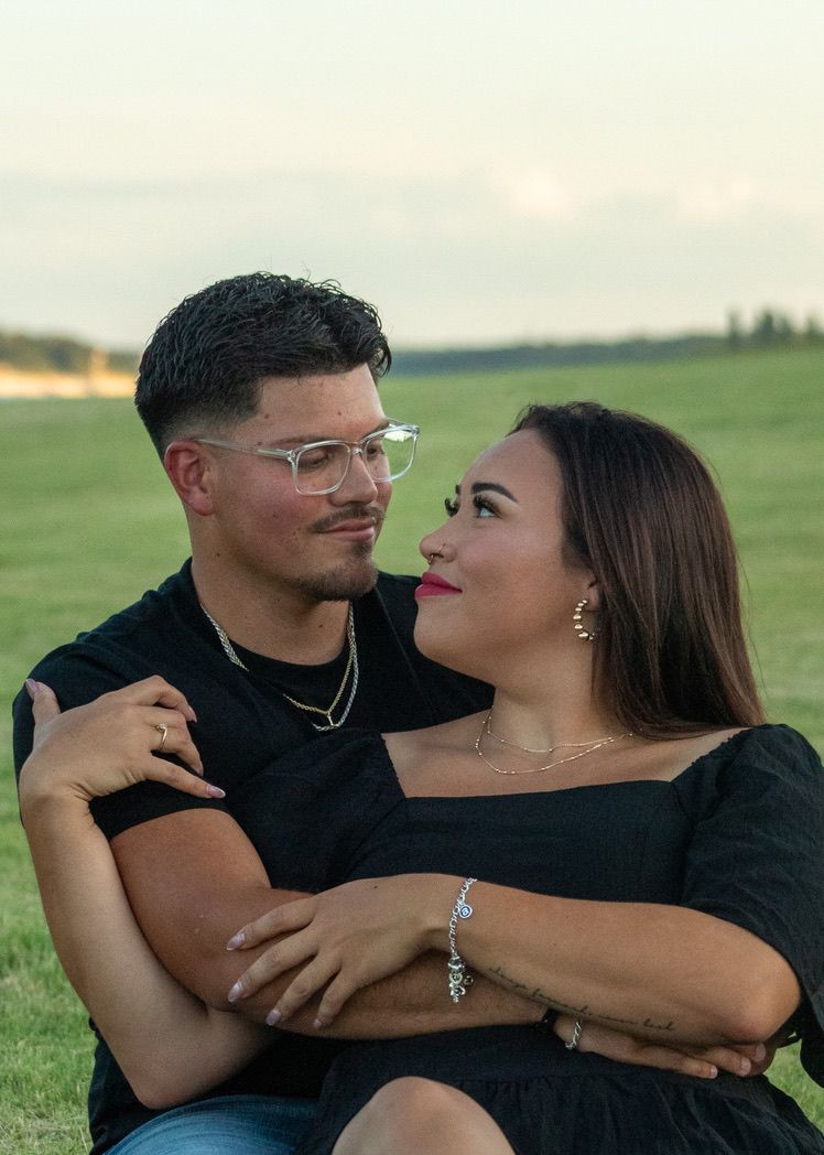 A couple share intimate moments in a grassy field wearing coordinated black outfits at sunset.