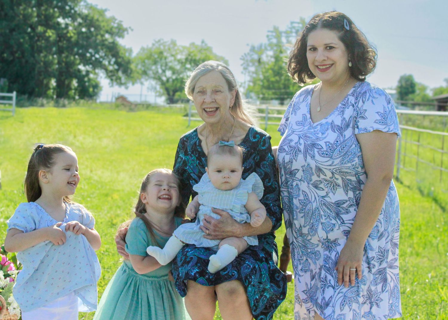 A joyful outdoor family photo session in a sunny green field with floral dresses and casual attire.