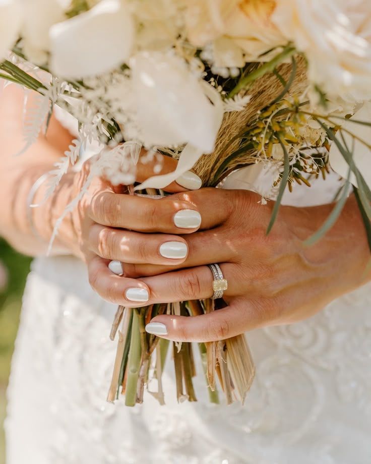 Close-up shot of bride's hands with white nail polish holding delicate floral wedding bouquet.