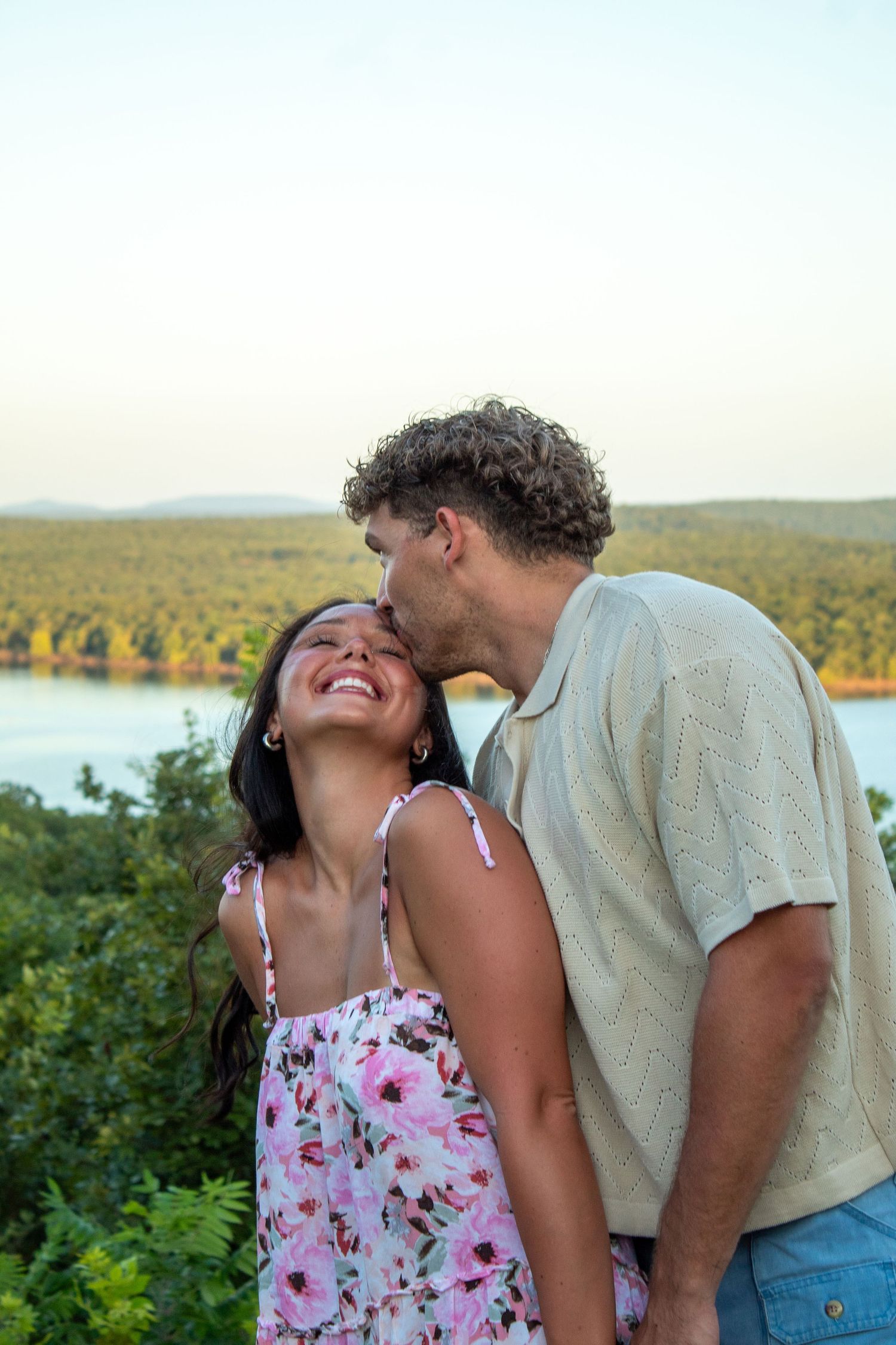 A romantic couple shares tender moments by a scenic lake overlook at sunset.