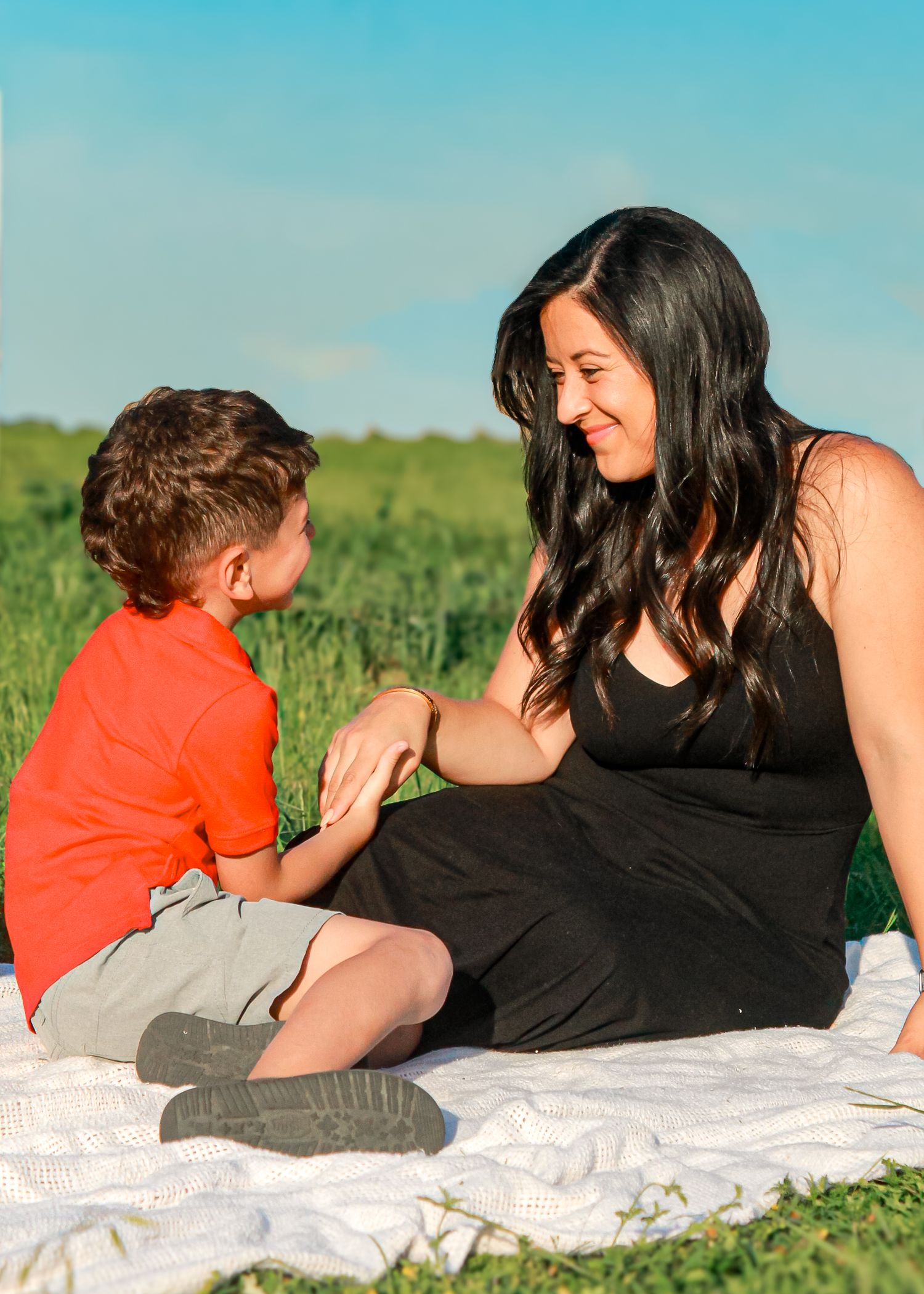 Family relaxing together on a white blanket in a grassy field on a bright sunny day.