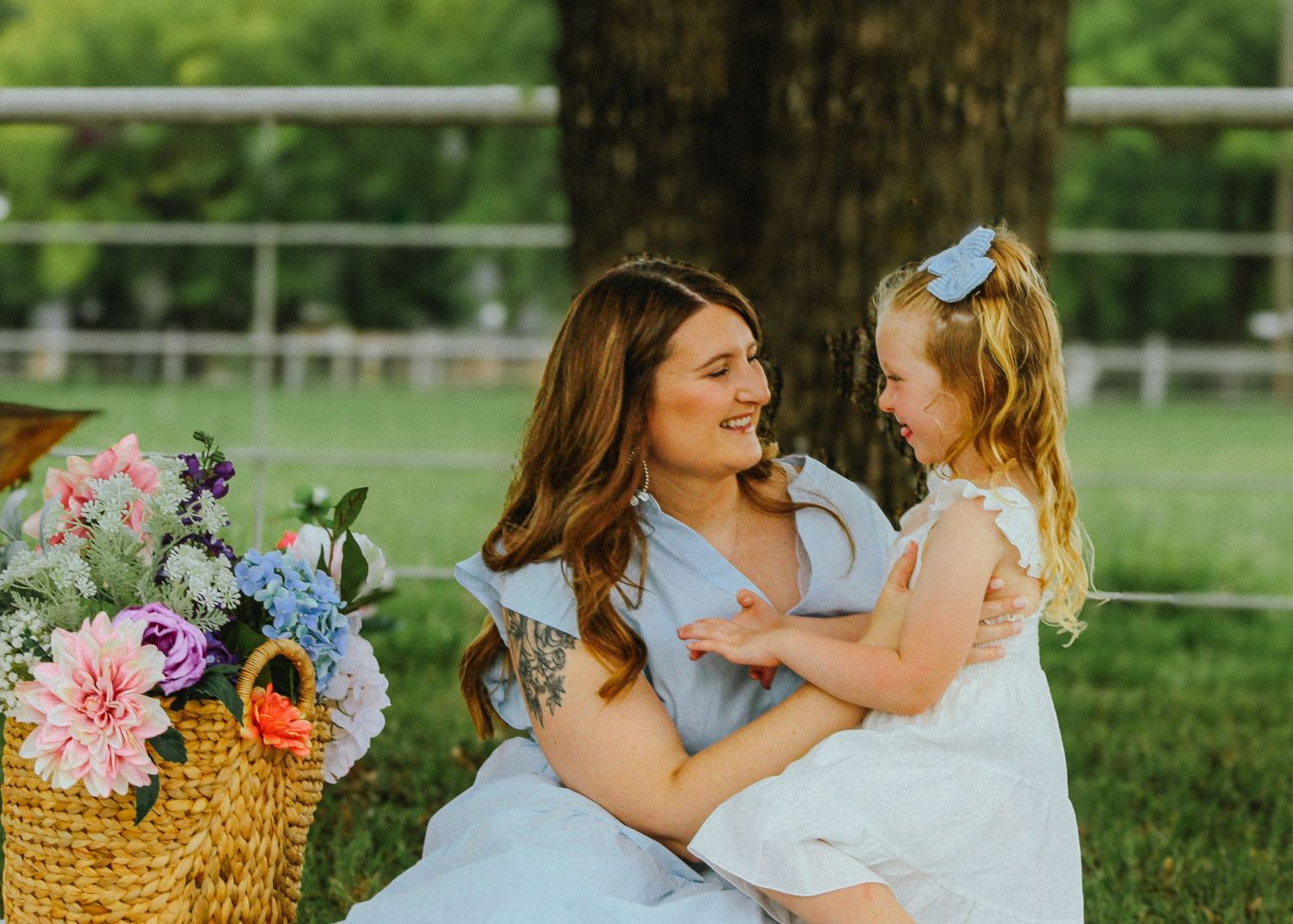 Mother and daughter in coordinating blue and white outfits share loving moment by flower basket.
