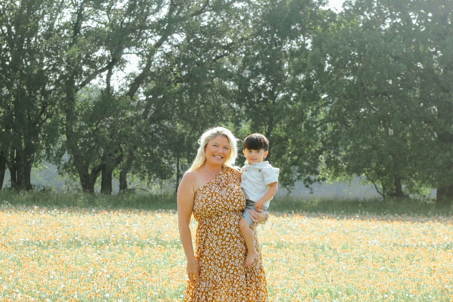 People walking through a sunlit meadow filled with yellow and white wildflowers.