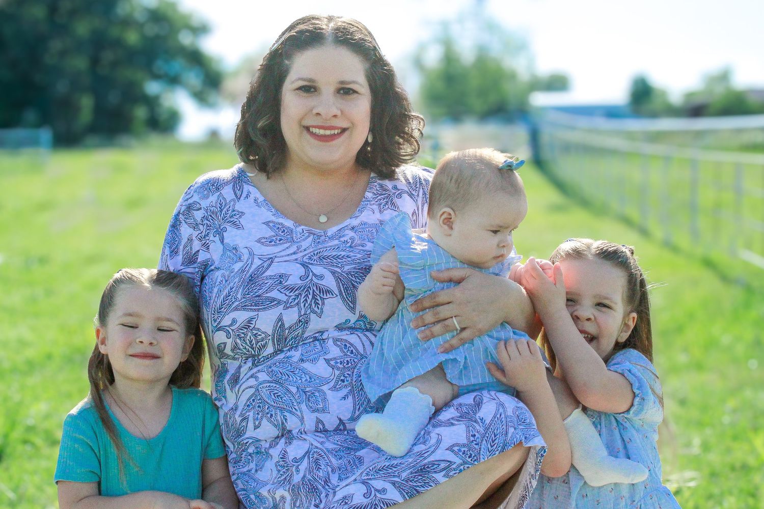 A cheerful family group photo on grass with three children and matching blue floral outfits.