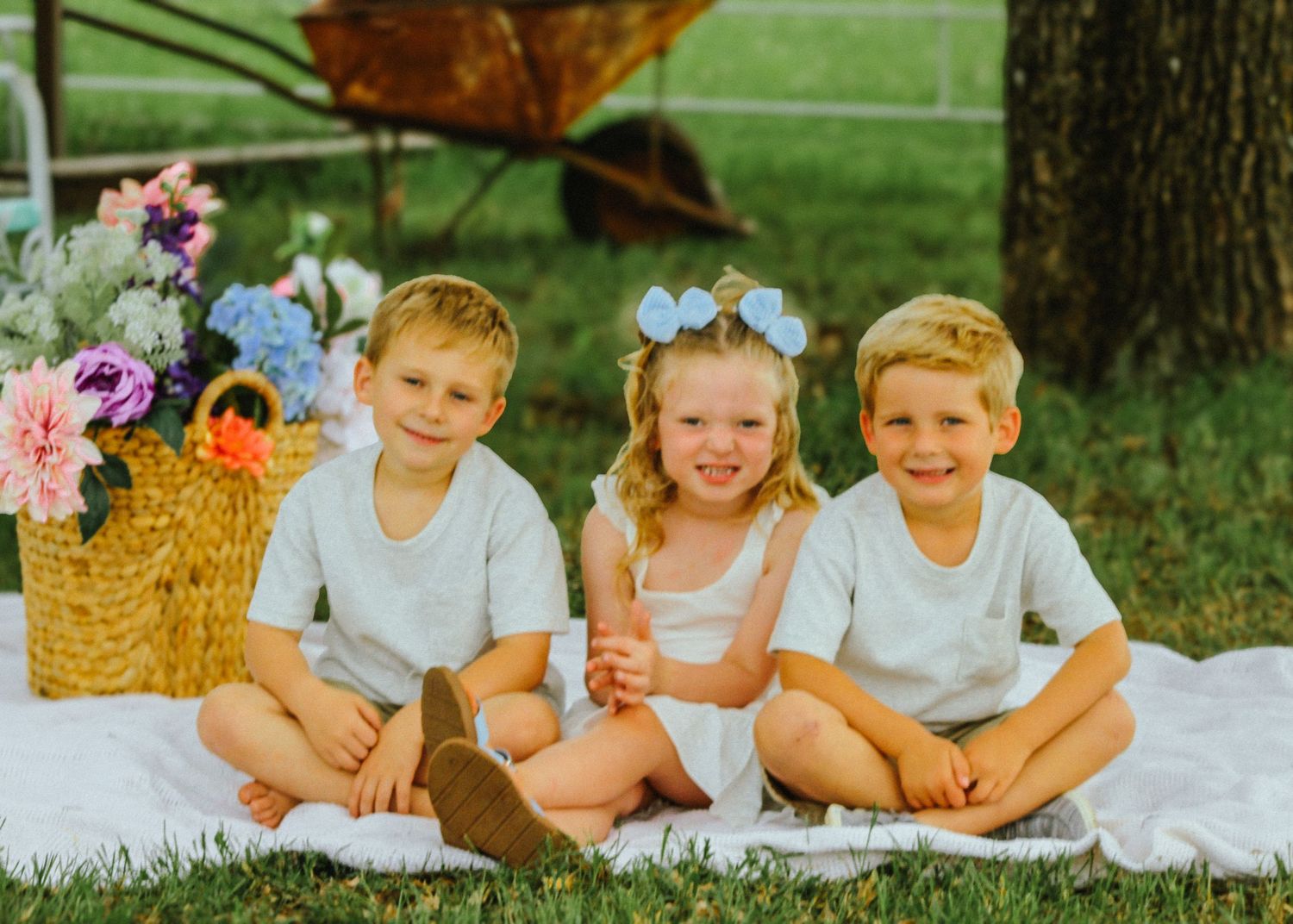 Children posed together on white blanket during outdoor photoshoot.