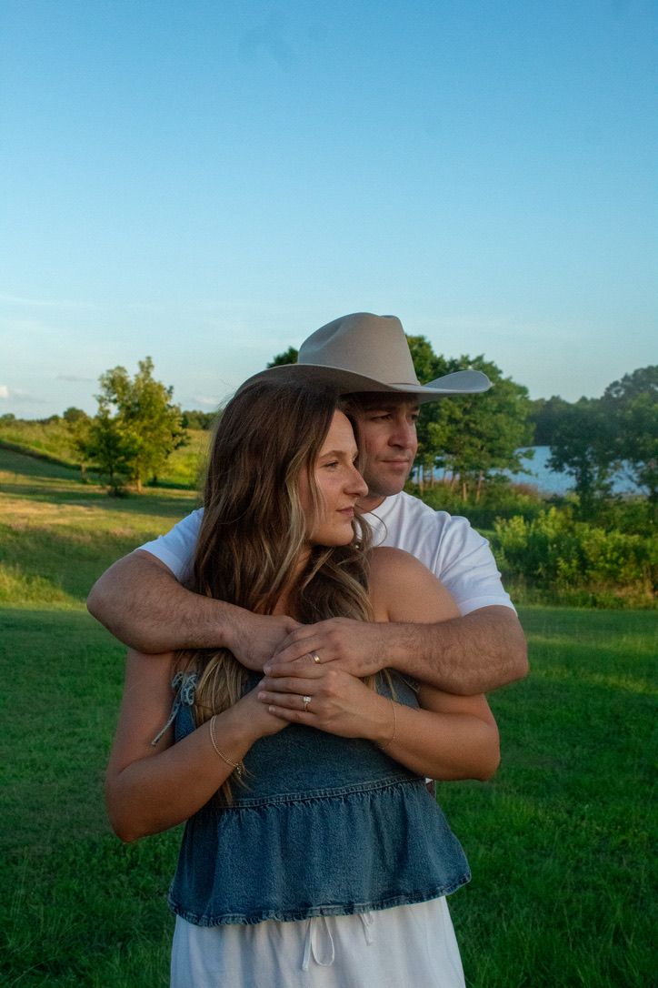 A couple embraces in a grassy field on a sunny afternoon.