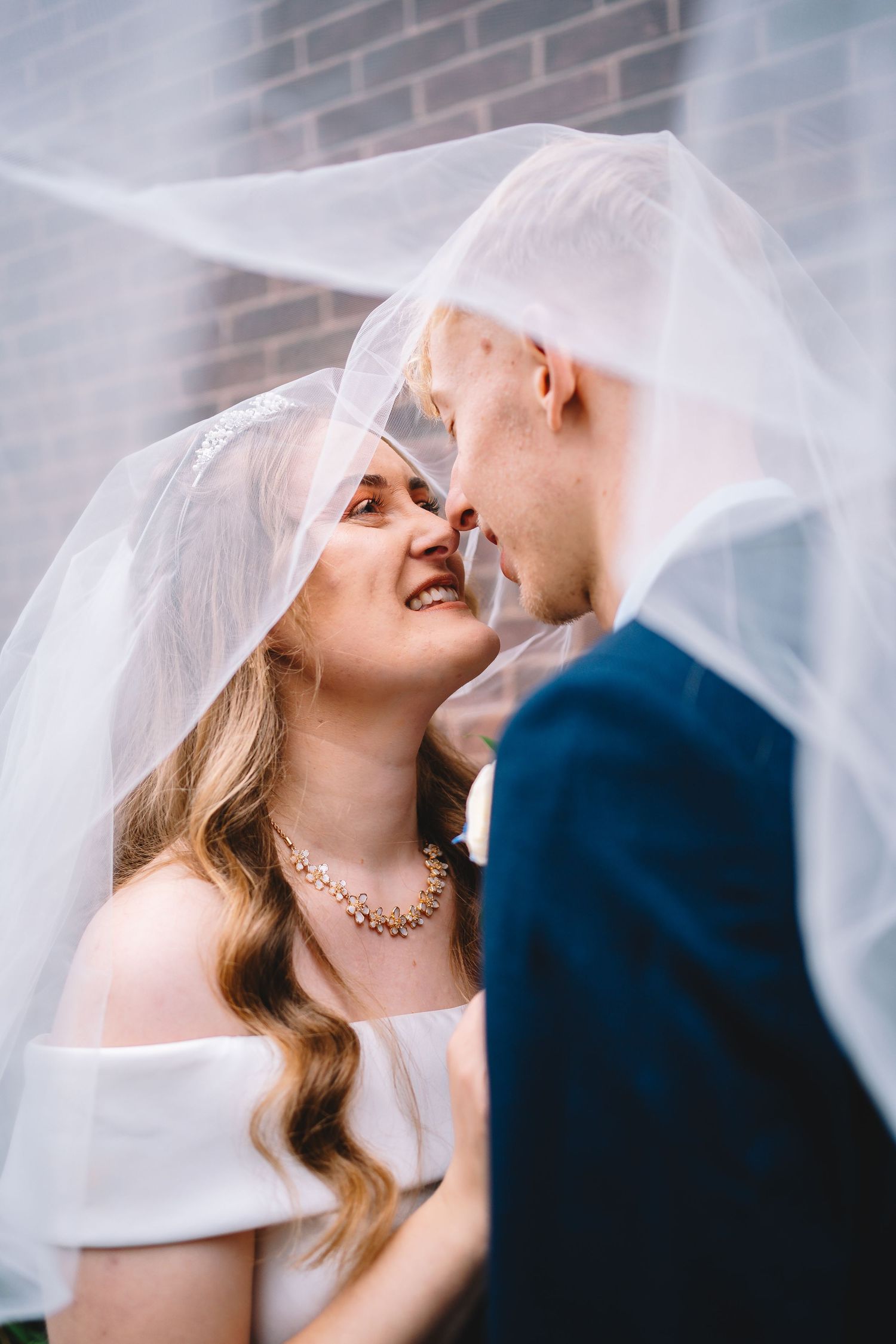 Creative wedding portrait of a bride and groom framed through fabric with soft light and intimate composition.