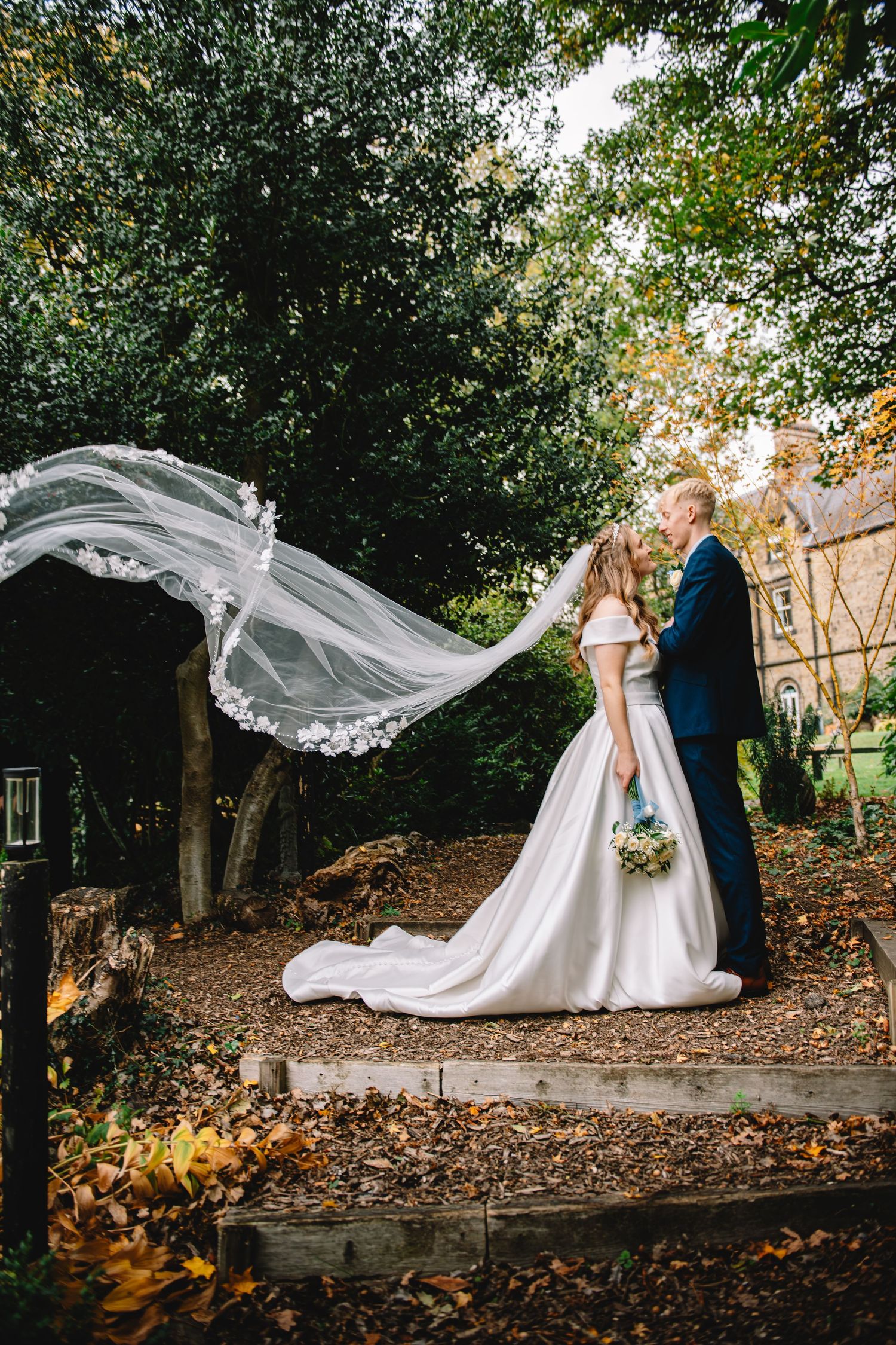 Bride and groom holding hands outdoors beneath a tree during a romantic wedding portrait session.