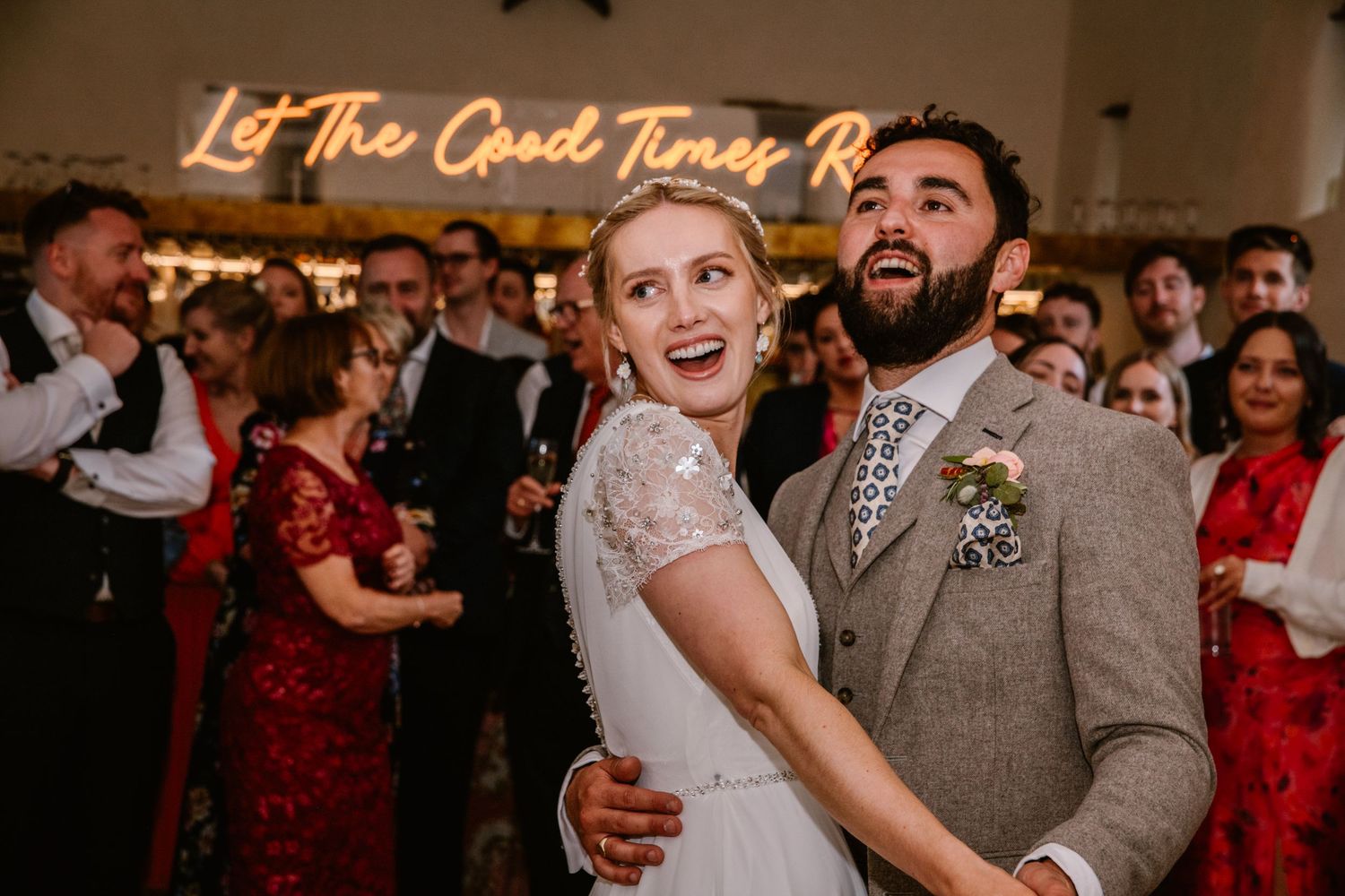 Joyful bride and groom share first dance at wedding reception with neon sign reading Let The Good Times Roll.