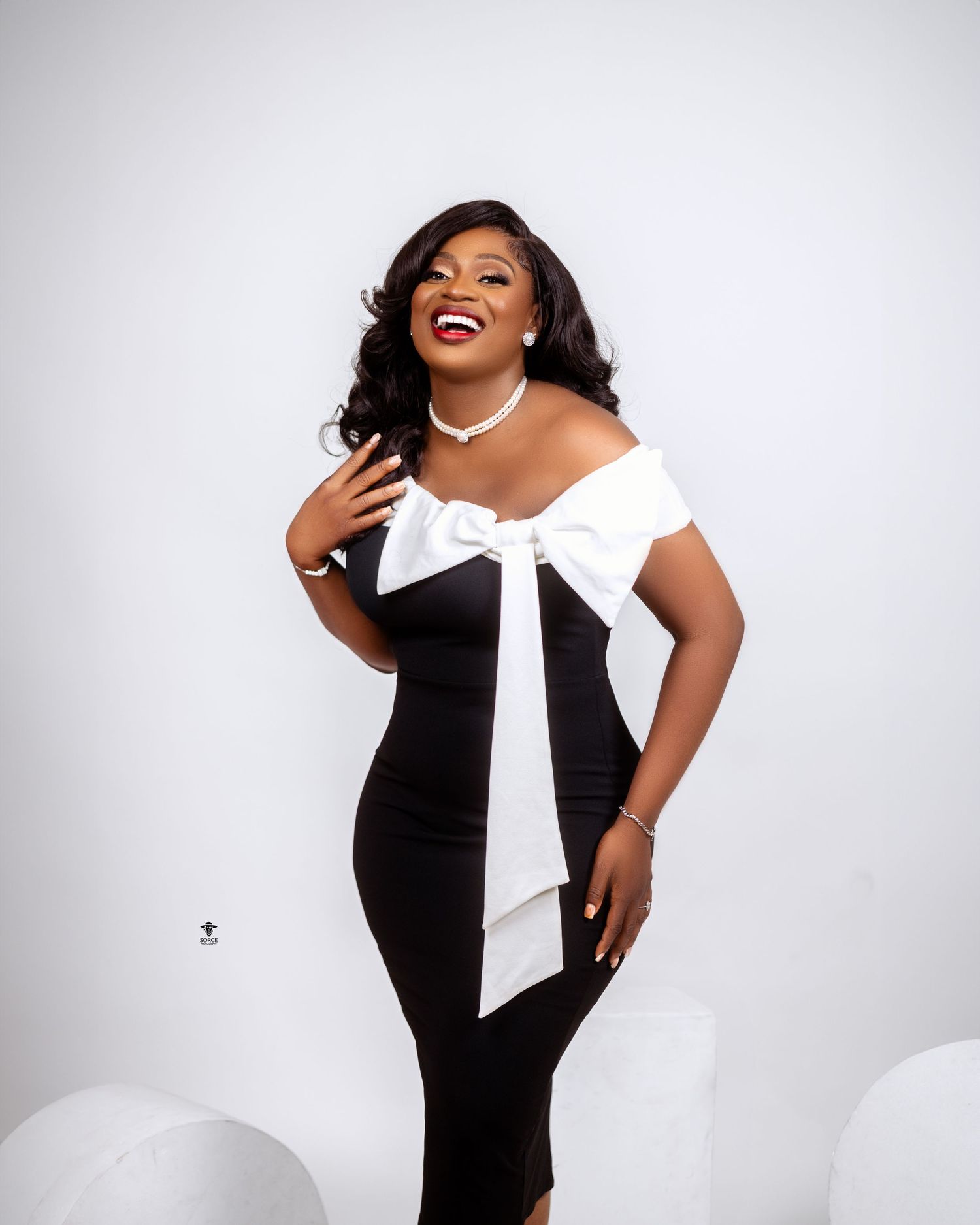 A figure in an elegant black and white dress poses expressively against a white backdrop, showing joyful movement.