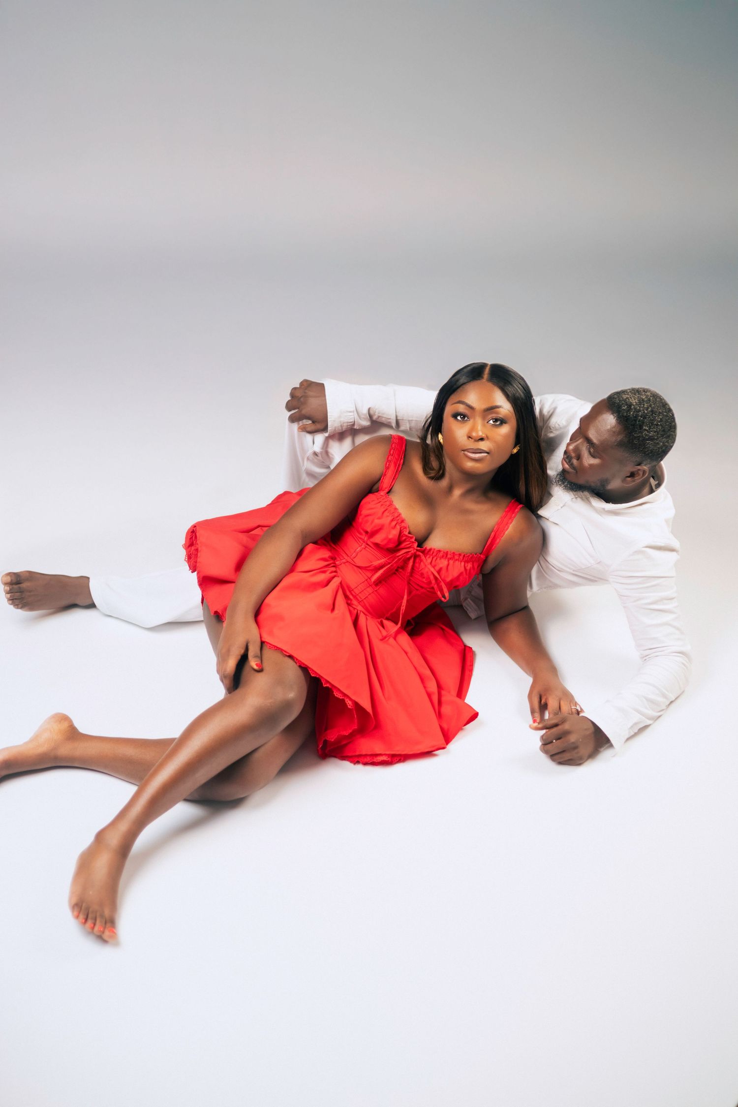 Couple in a romantic pose on a white background, with woman in red dress and man in white outfit.