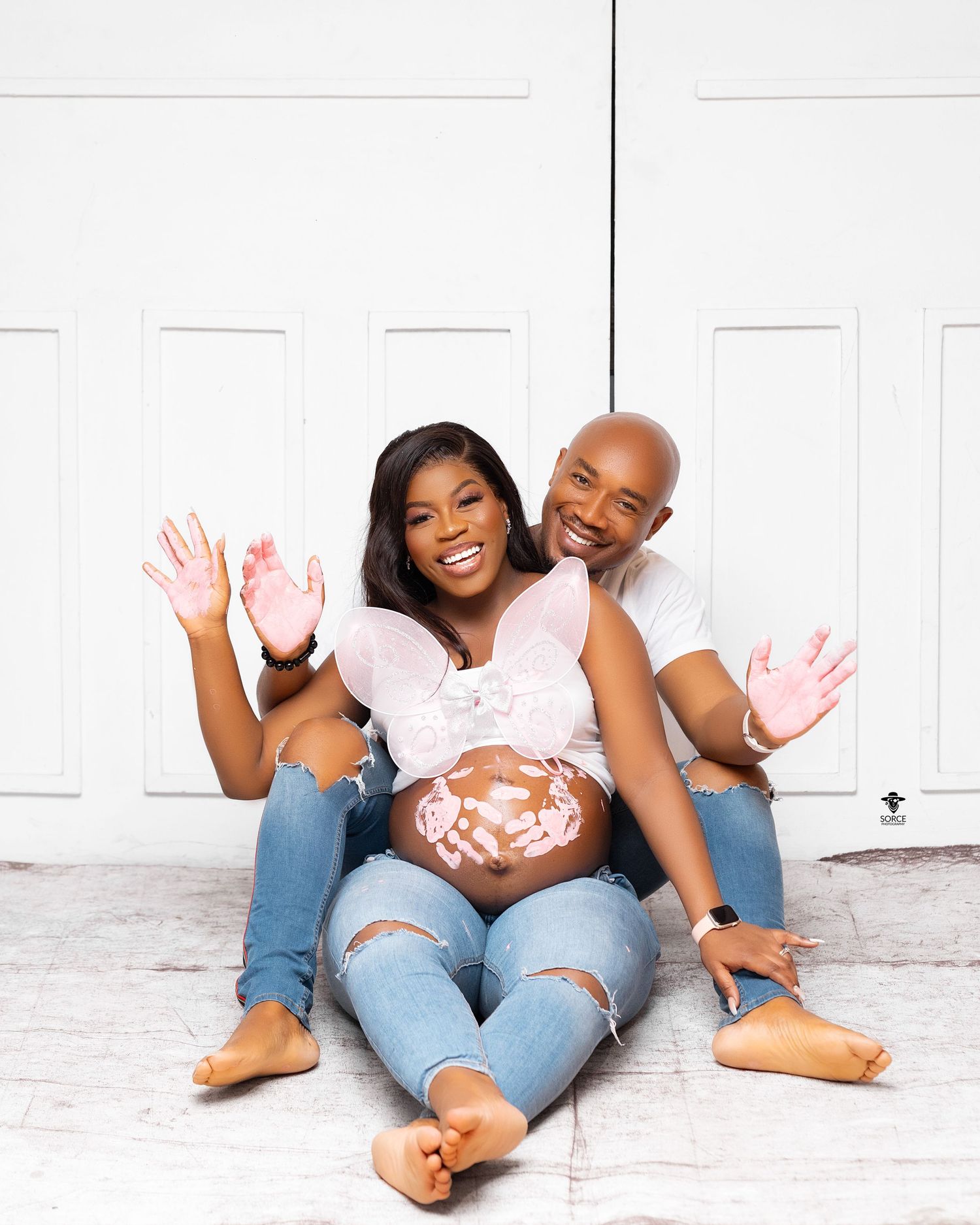 Loving couple shares playful and intimate barefoot moments in casual denim while laying on a white floor.