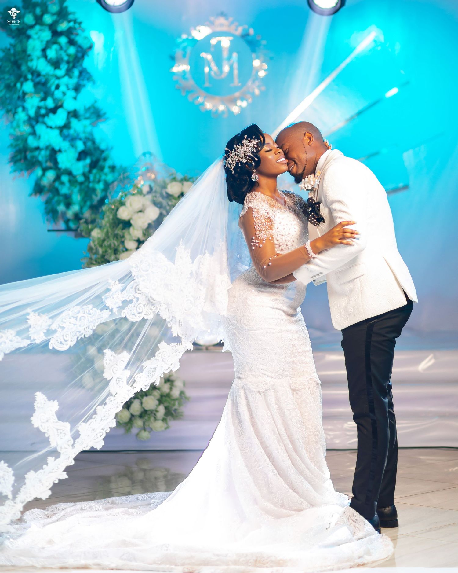 Couple in formal attire slow dances under blue lighting during what appears to be their wedding reception.