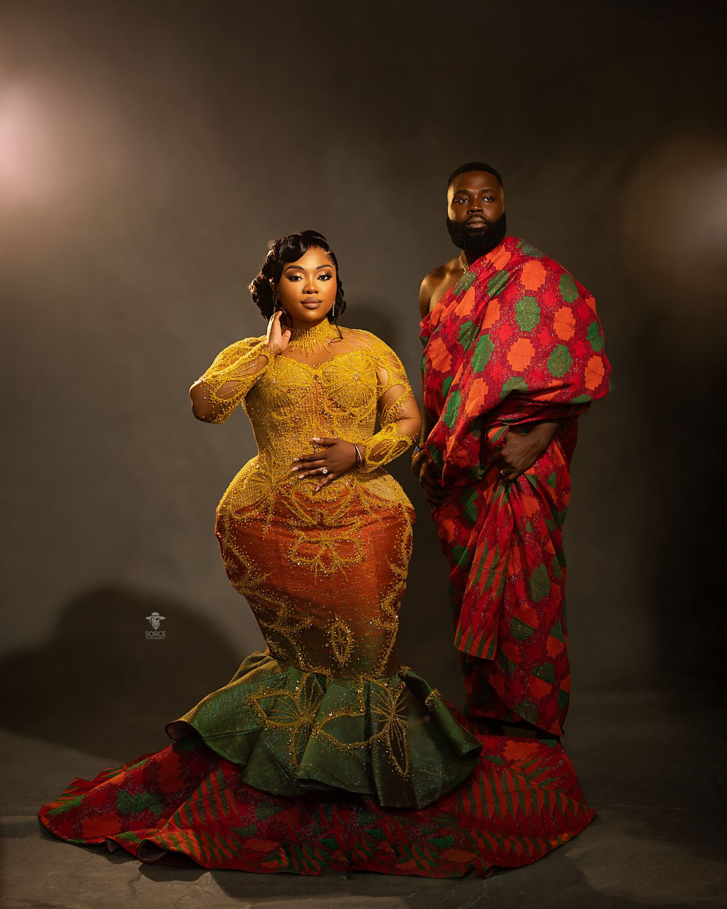 Two performers in vibrant red and yellow flowing costumes dance expressively against a dark backdrop in a studio setting.