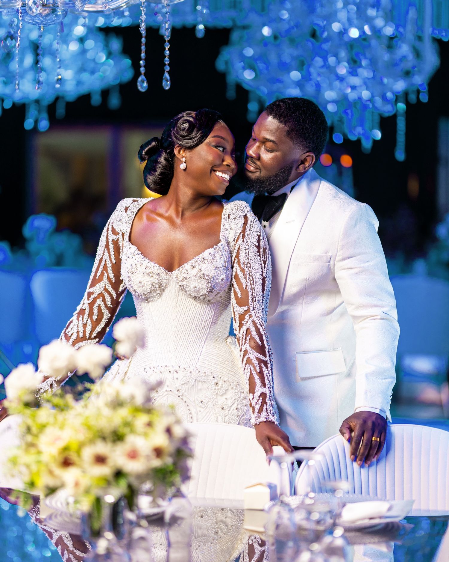 Elegant couple in wedding attire sharing a romantic moment at a luxurious blue-themed reception with crystal chandeliers.