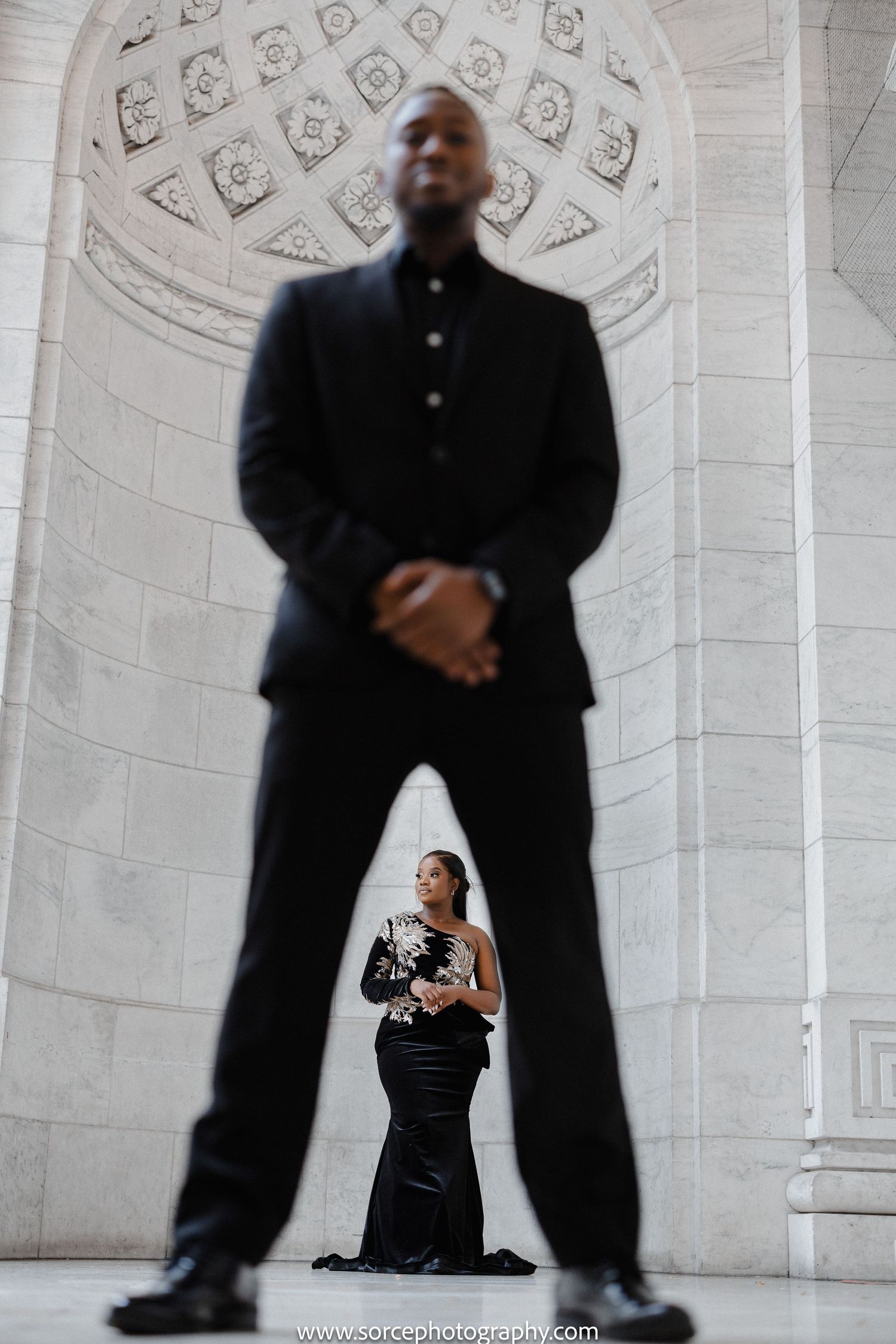 Creative wedding photography perspective with a dramatic contrast between two people posing in an ornate white hall.