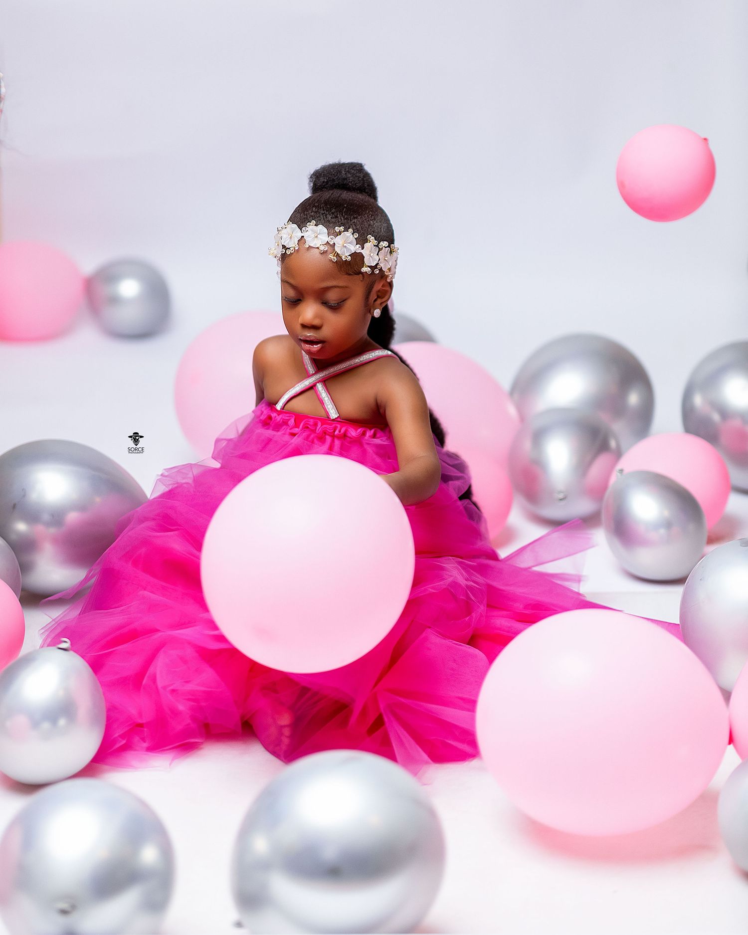 Artistic photoshoot featuring hot pink tulle dress and metallic silver and pink balloons against white backdrop.