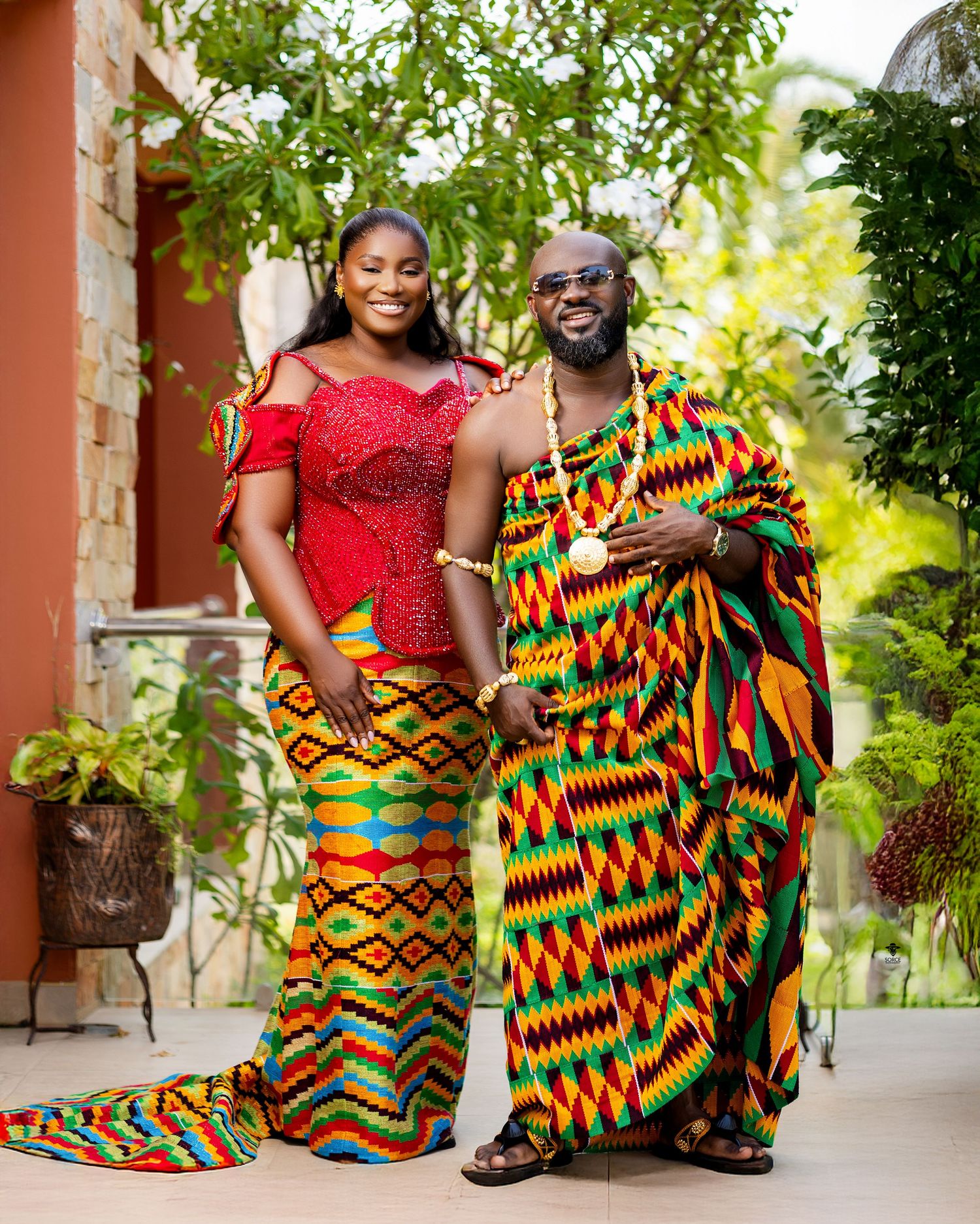Couple in vibrant Kente cloth traditional Ghanaian attire posing together outdoors at a cultural celebration.
