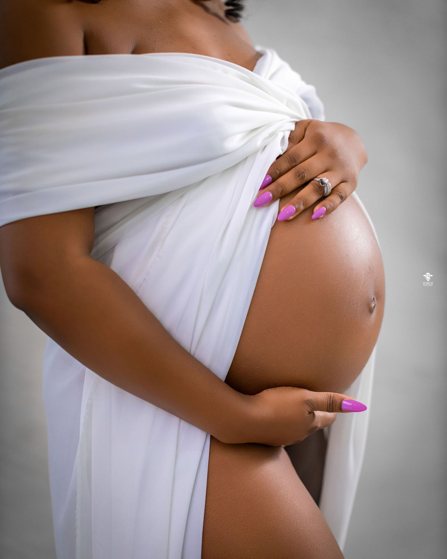 A series of maternity photos showing a pregnant belly draped in soft white fabric against a dark background.