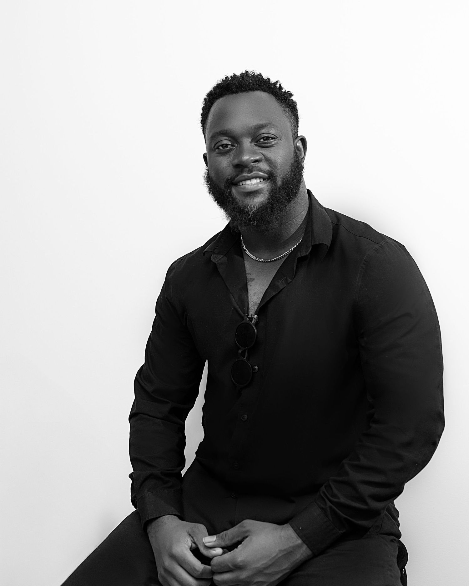 Professional portrait of person in black attire smiling and posing against a white background.
