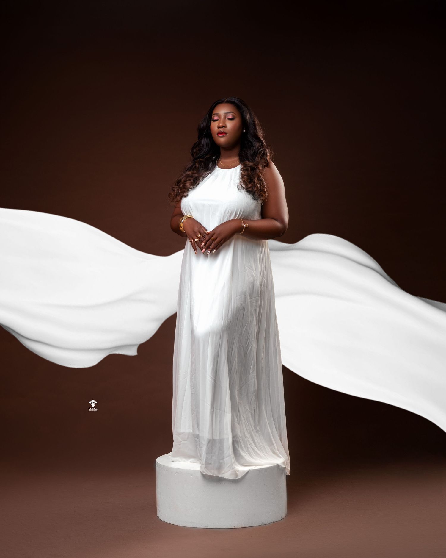 A flowing white dress billows dramatically against a dark brown background in an artistic fashion photograph.