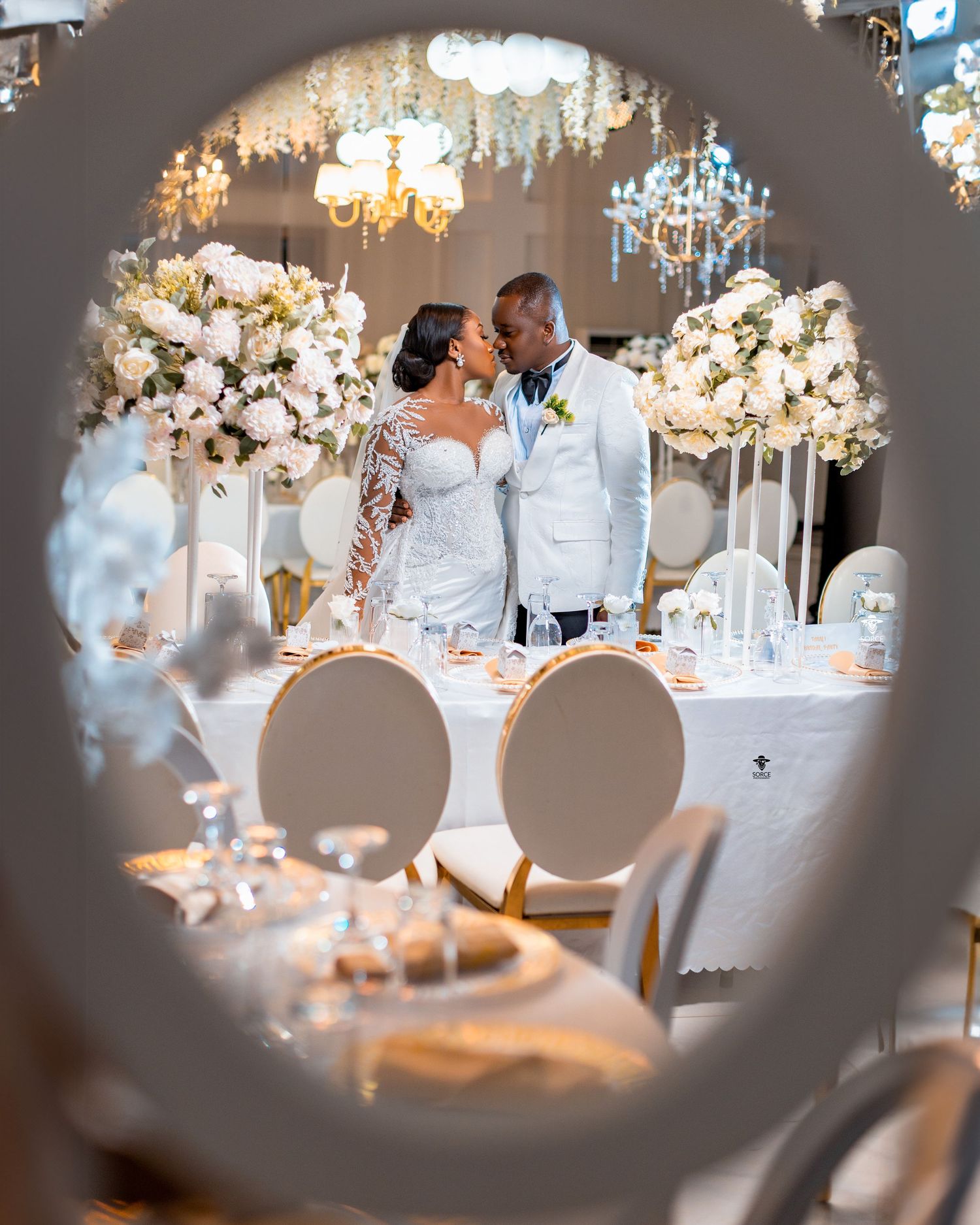Elegant wedding reception venue decorated with crystal chandeliers and formal table settings in soft lighting.