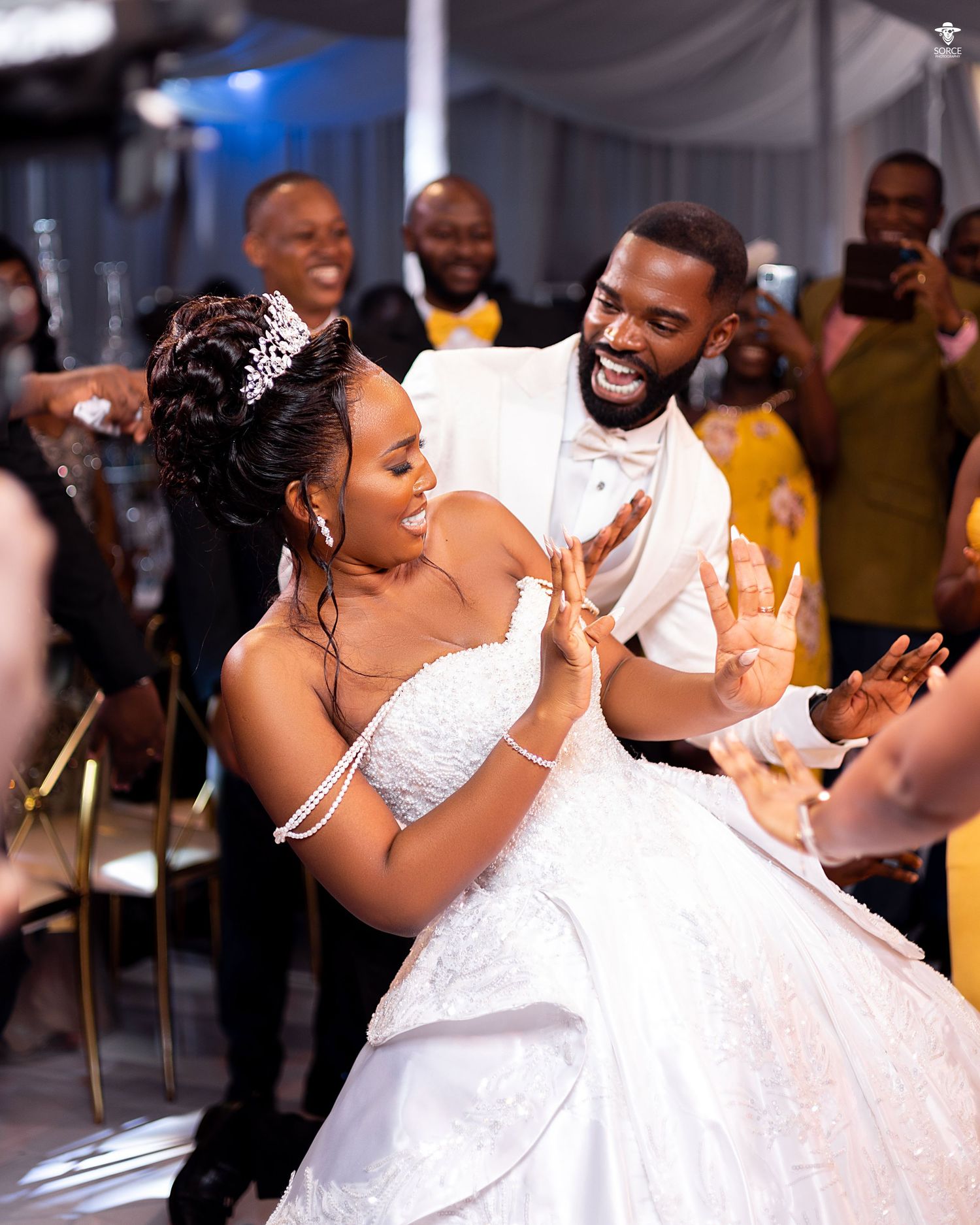 A couple shares a romantic moment dancing together at a wedding reception with guests looking on in the background.