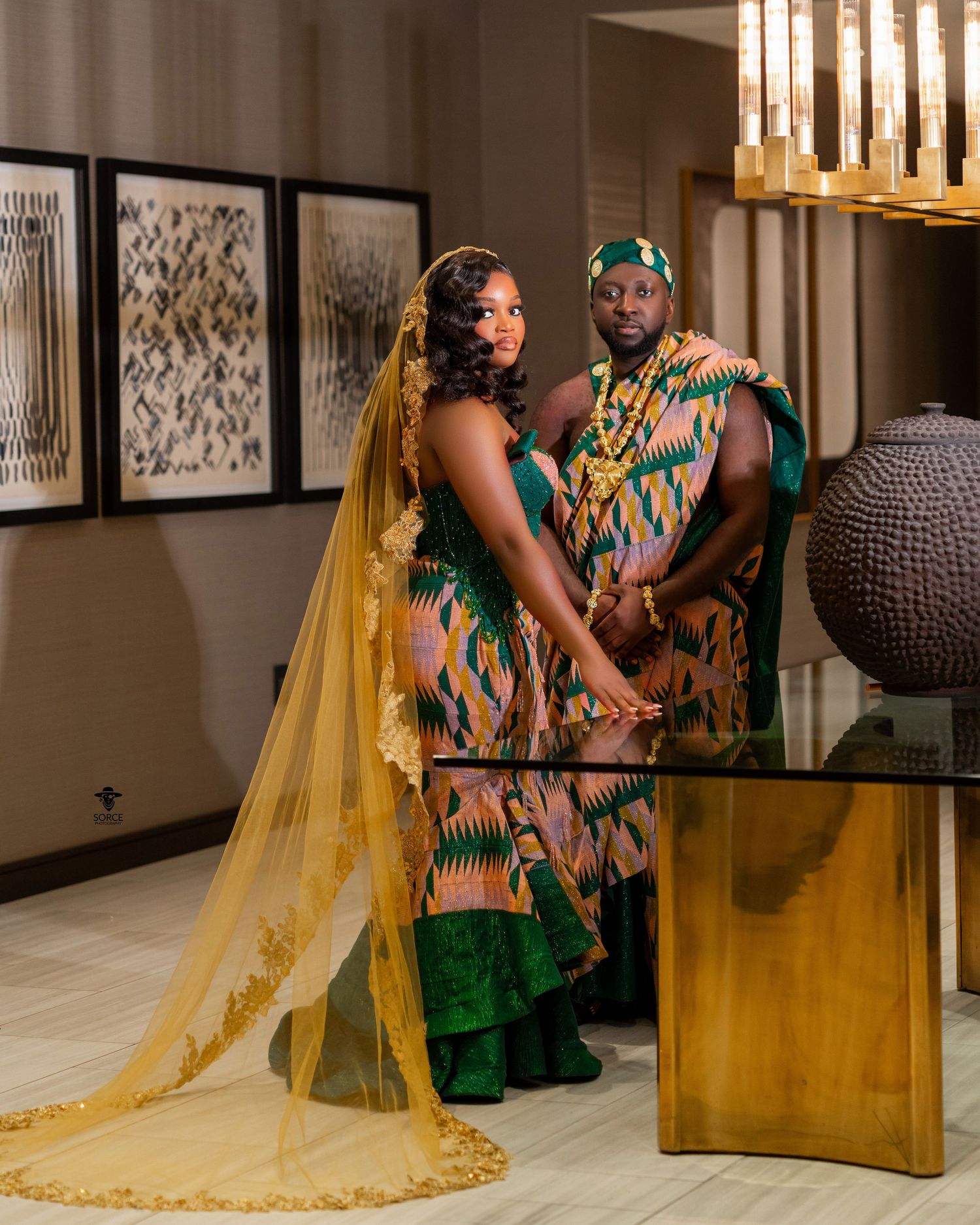 A couple in traditional African attire with yellow and green kente fabric pose together during a formal photo session.