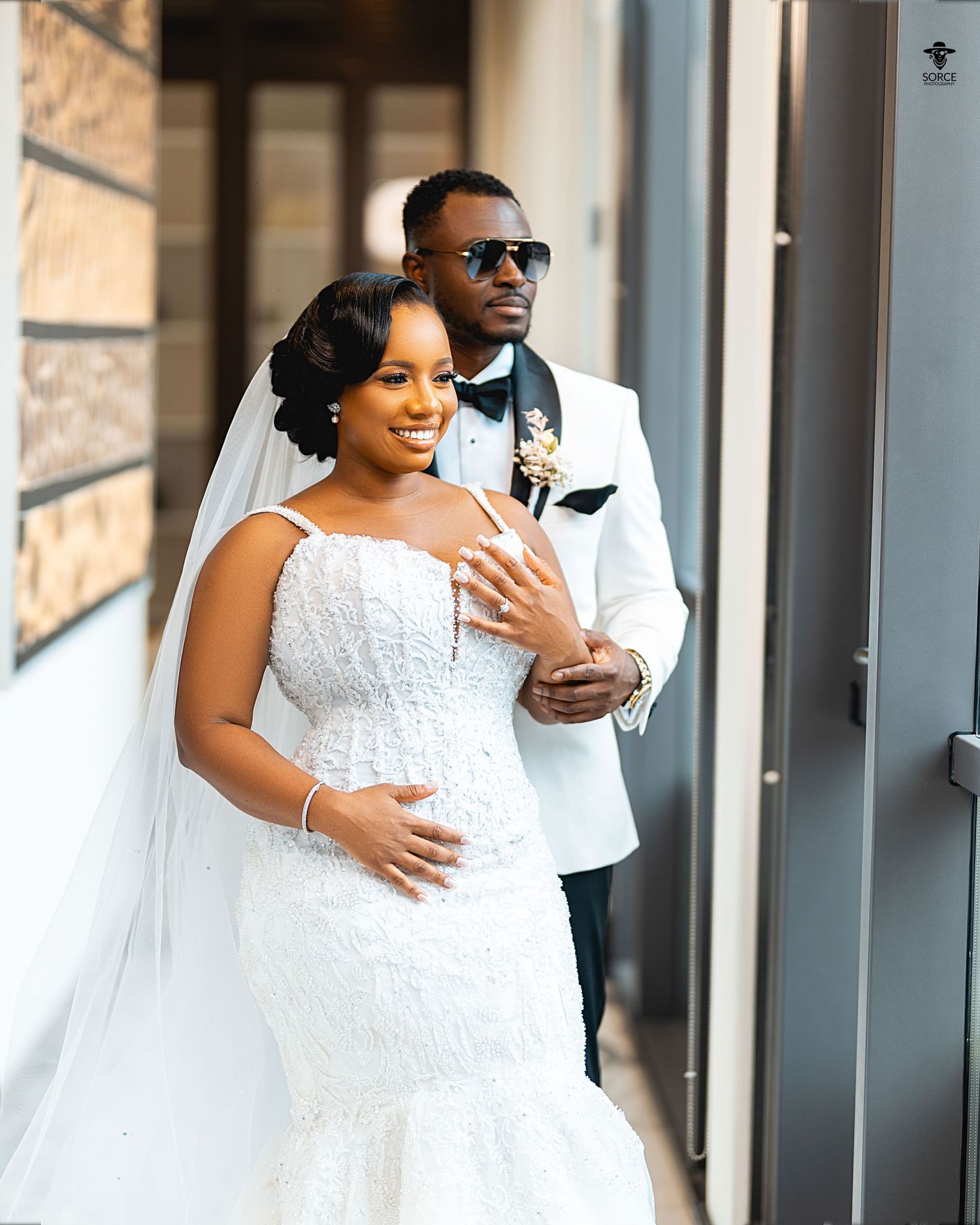 Bride and groom embrace in front of windows during romantic indoor wedding photo session.