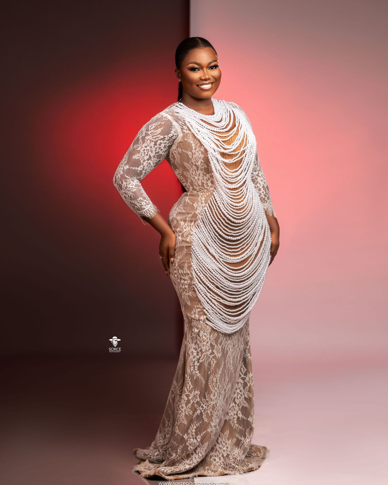 A figure in a lace dress with dramatic pearl neckpiece poses gracefully against a red and pink gradient backdrop.