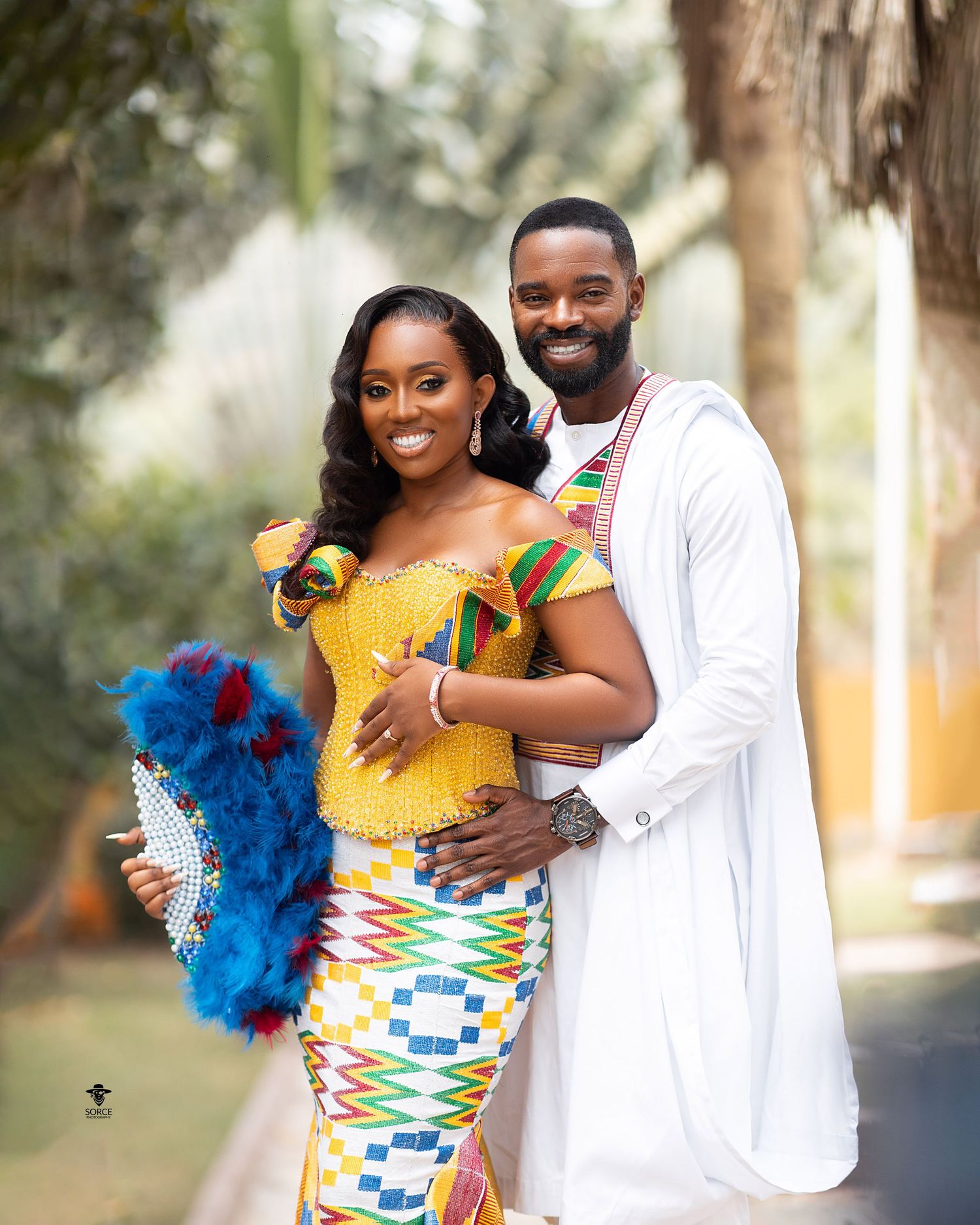A couple in traditional African kente print attire embracing outdoors in a romantic photoshoot.