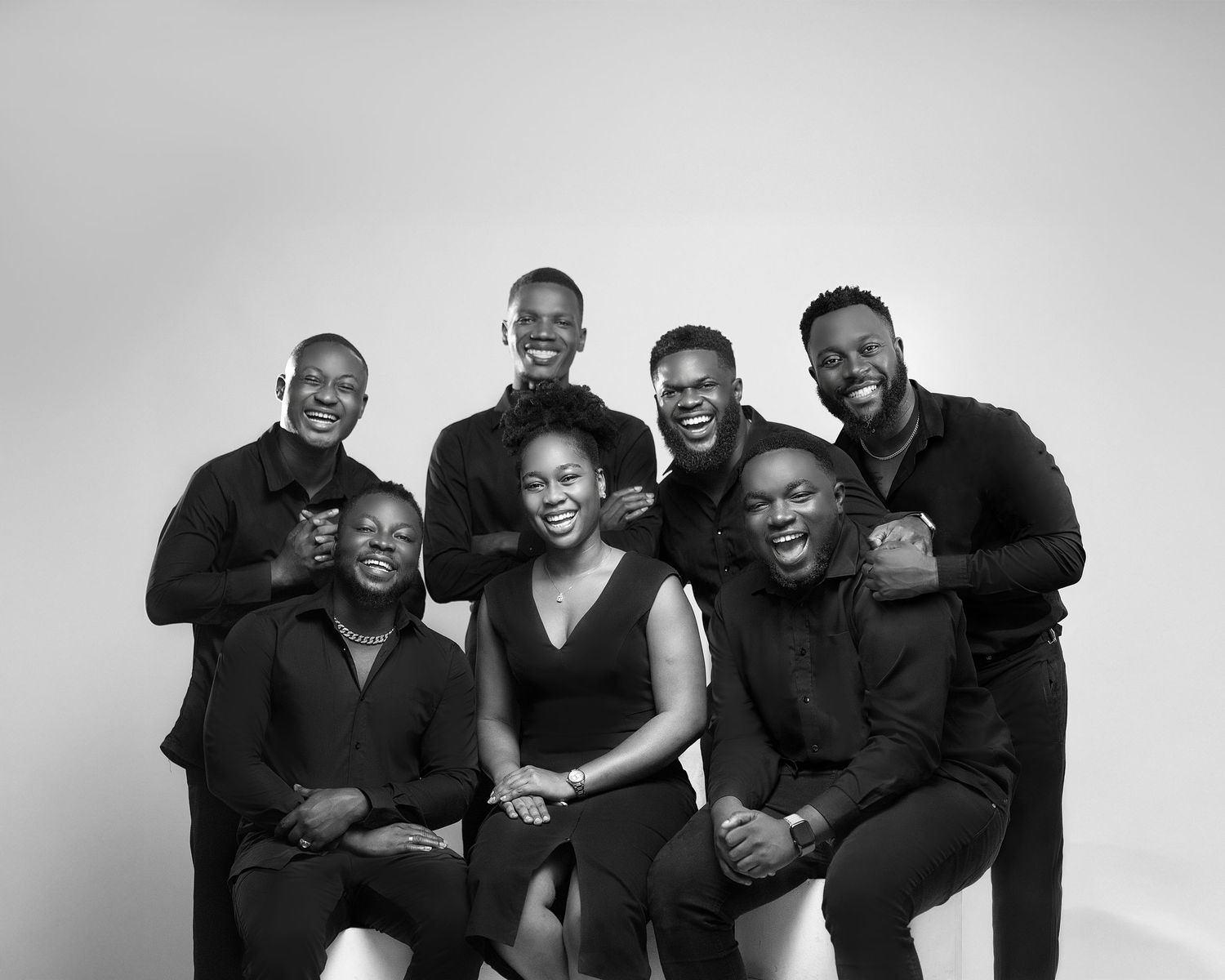 A series of black and white portraits showing a group in coordinated black outfits posing playfully together.