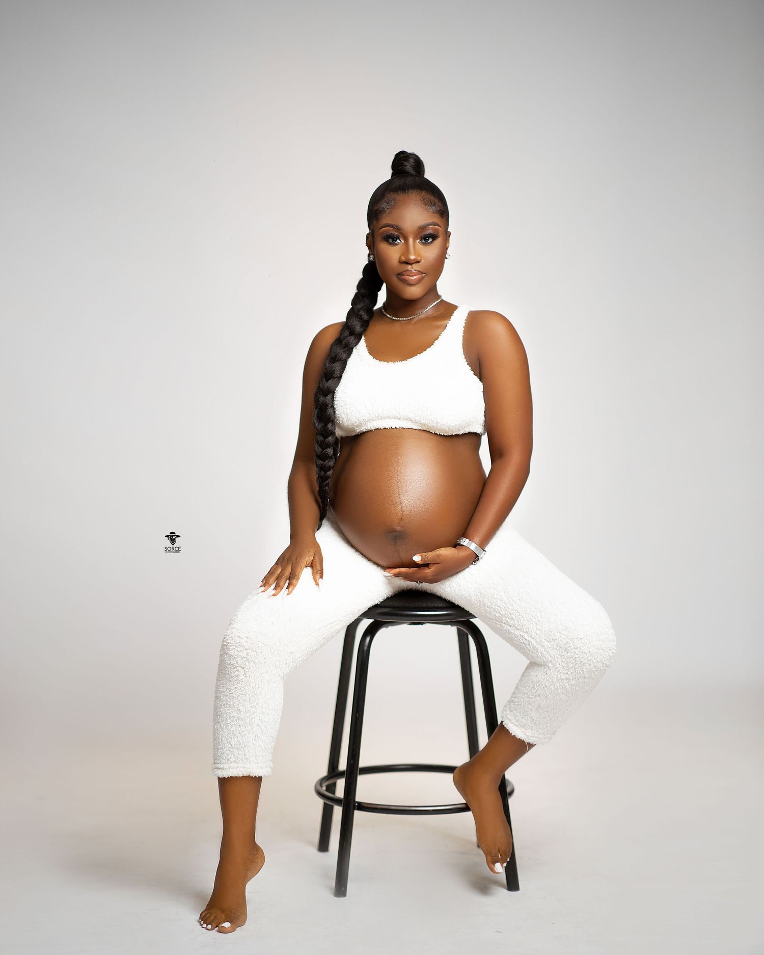 A maternity photoshoot series in a white studio featuring a seated pose in athletic wear against a light background.