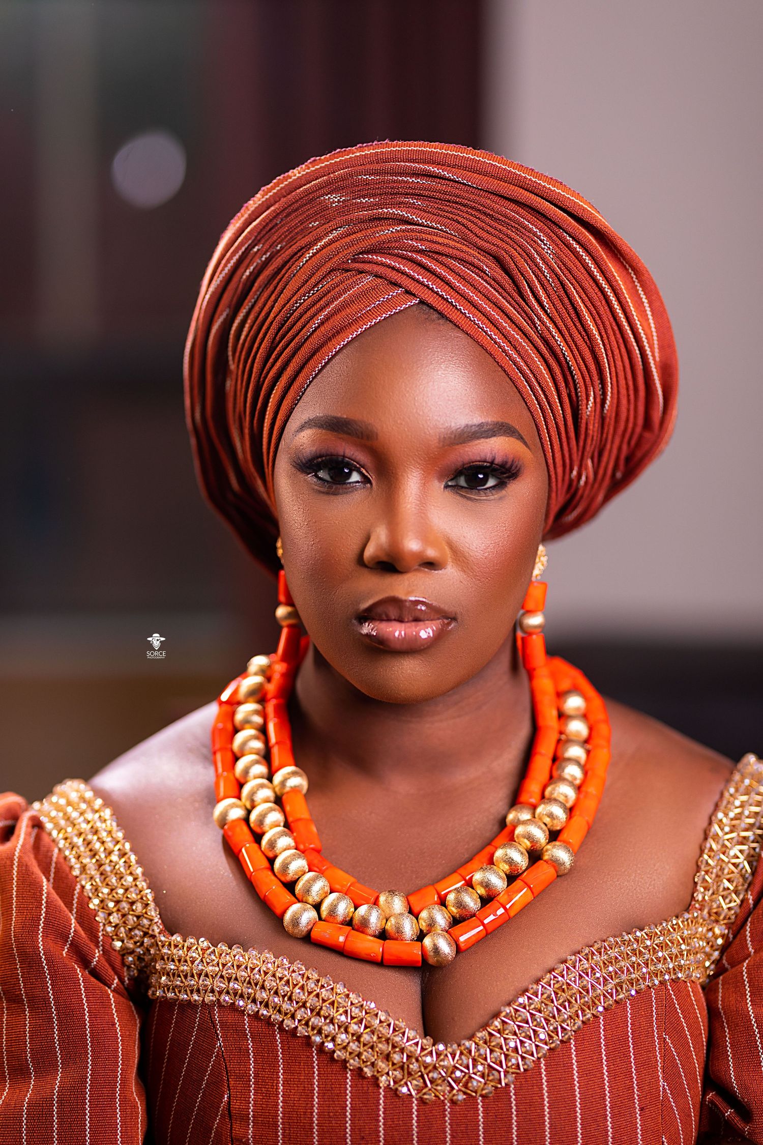 Traditional African attire showcasing orange and gold beaded jewelry with matching headwrap and elegant makeup.