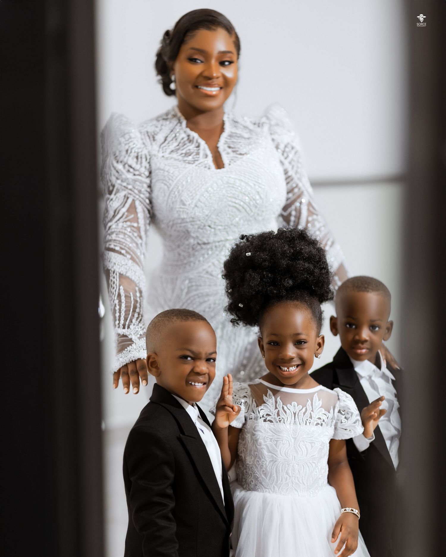 A formal family portrait shows a parent in white lace with three children dressed in black and white outfits.