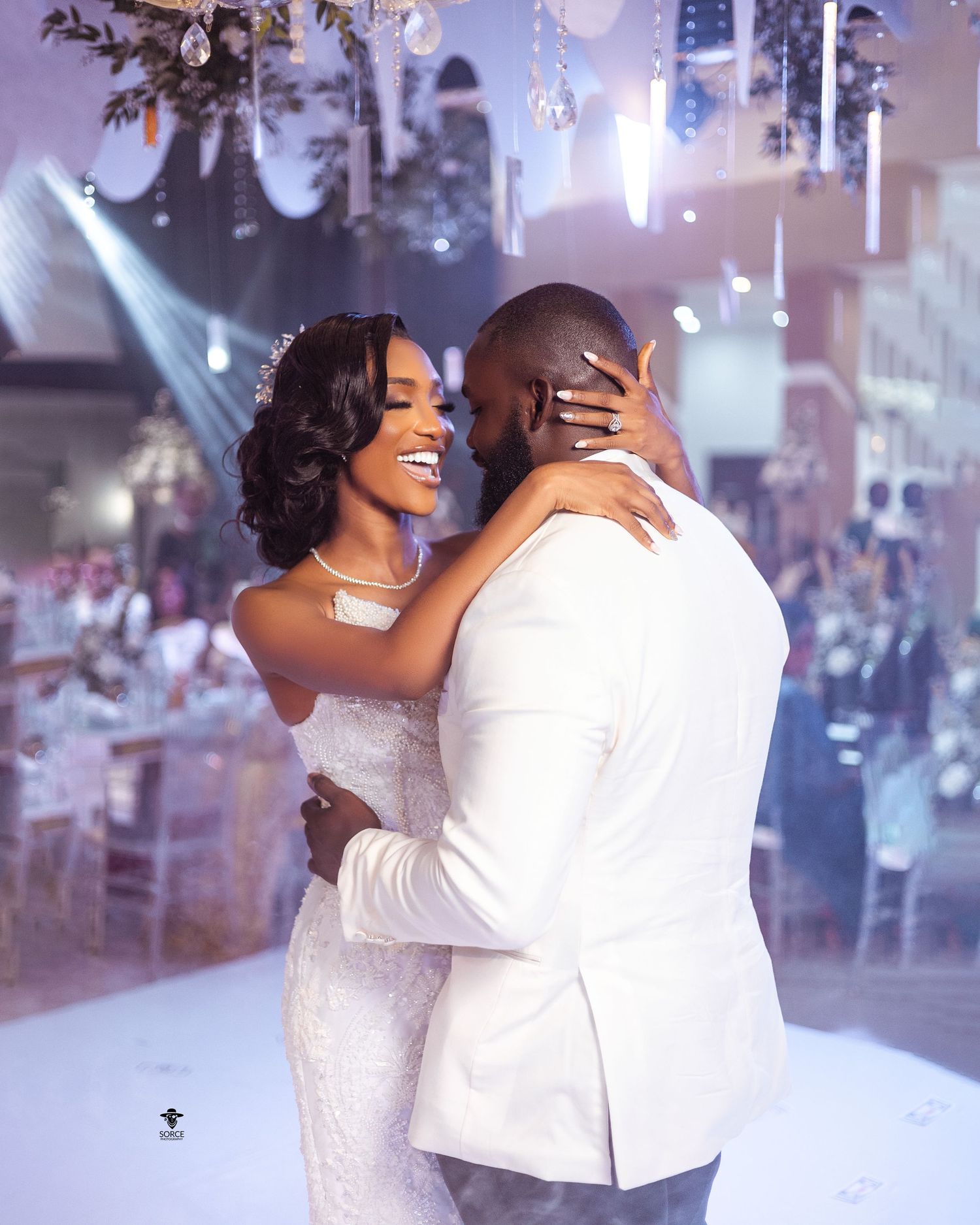 A couple embraces on the dance floor during their first dance at a wedding reception with dramatic lighting and decorations.