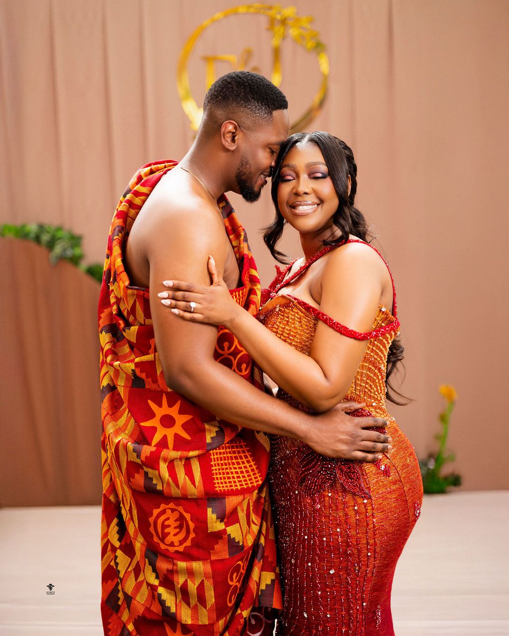 Couple in vibrant Kente cloth attire embracing warmly during a traditional Ghanaian engagement ceremony.