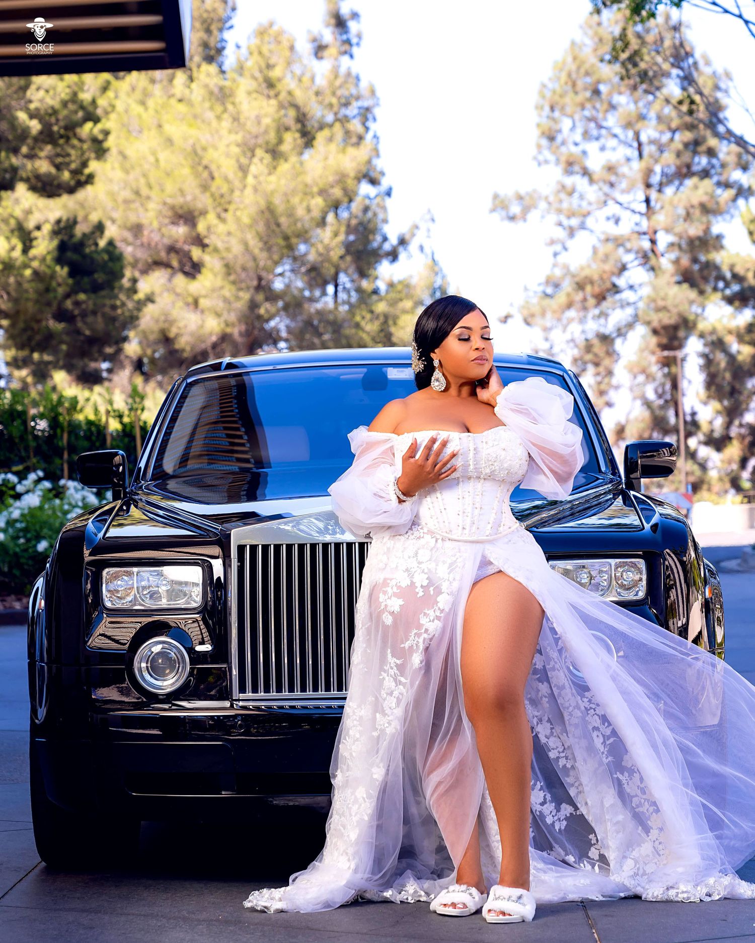 Stunning bride in lace gown poses with luxury Rolls Royce in dramatic outdoor photo shoot.