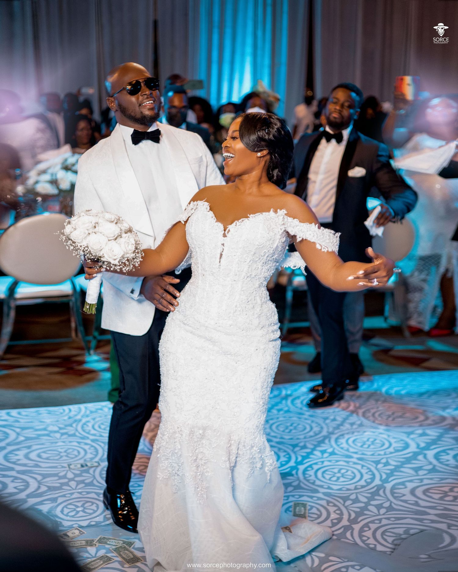 Newlyweds share a joyful dance moment on their wedding day with romantic blue lighting in the reception venue.