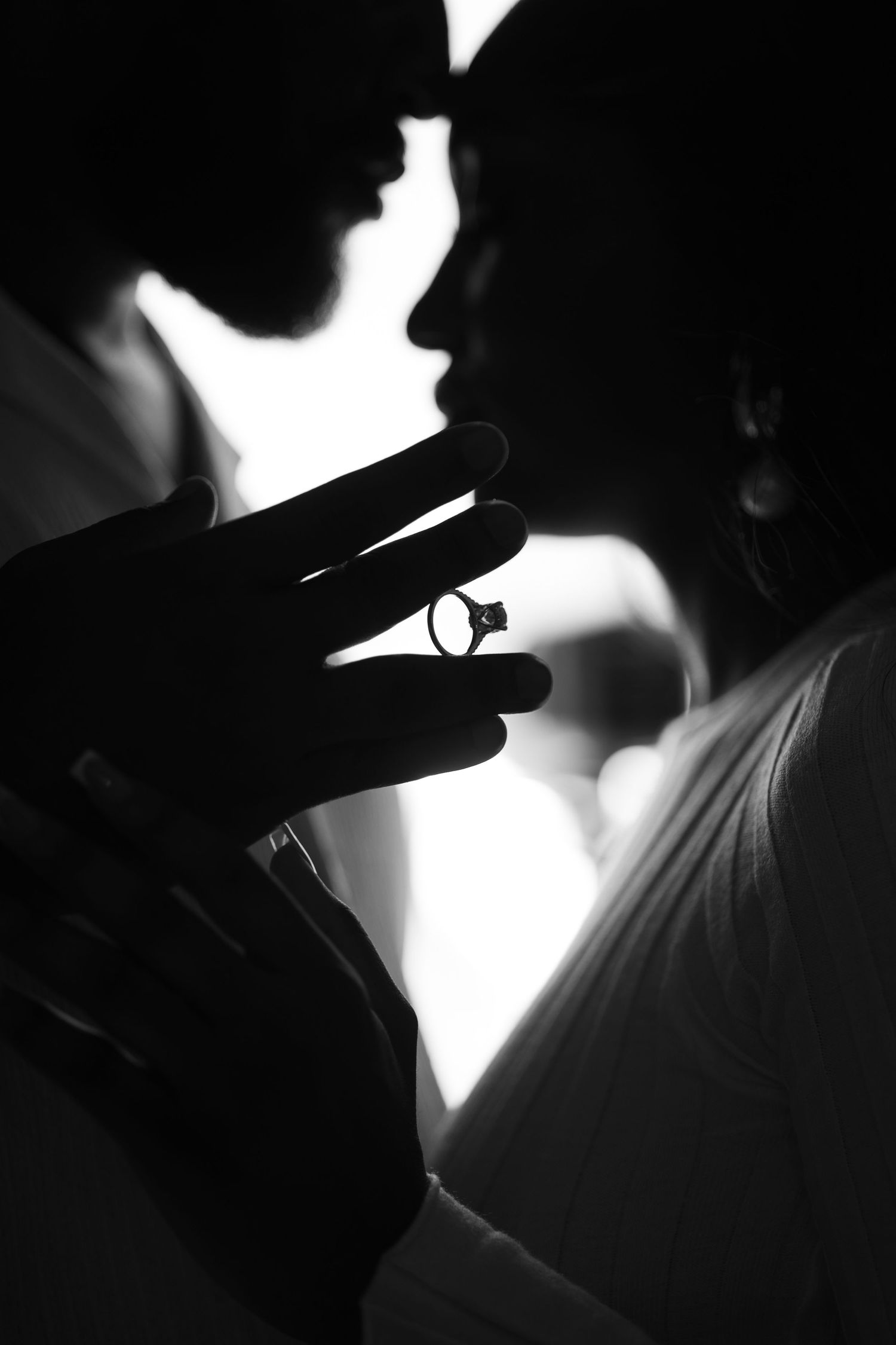 Dramatic black and white silhouette sequence shows a ring being held and rotated between fingers against bright background.