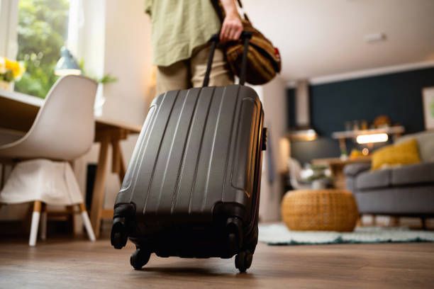 Black hardshell luggage suitcase shown from different angles on wooden floor in home setting.