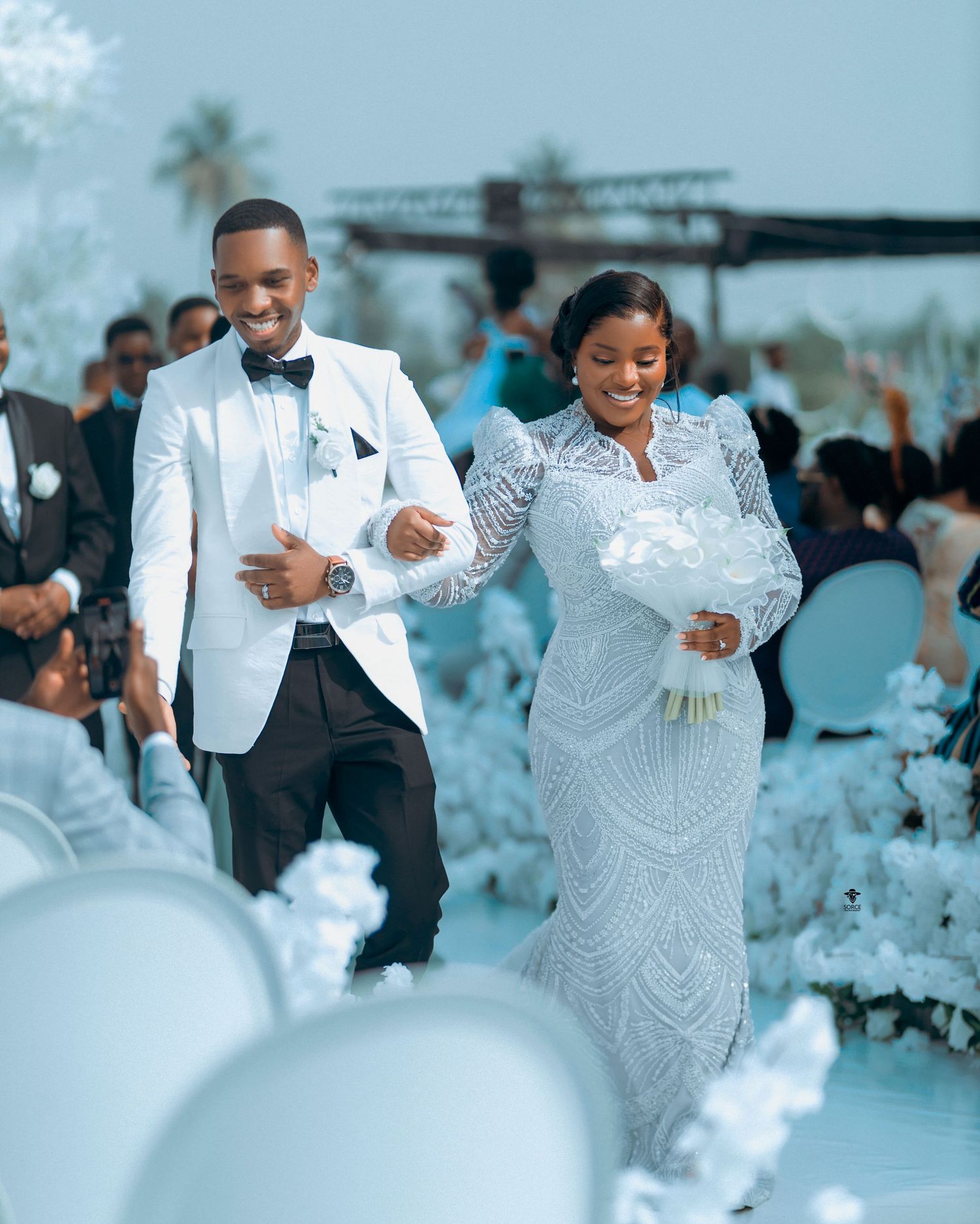 A couple shares a joyful dance at an elegant white-themed wedding reception with decor and floral arrangements.