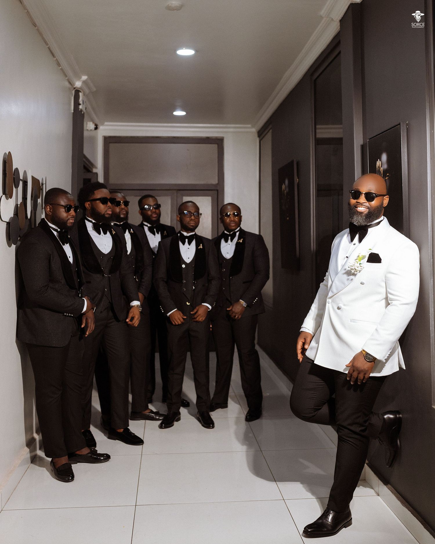 A creative split photo collage showing groomsmen in black suits posing along a white hallway from different angles.