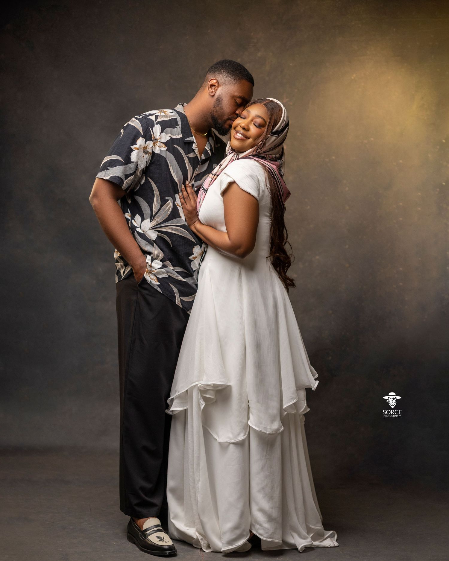 A couple shares a tender embrace during a romantic photoshoot against a dark dramatic backdrop.