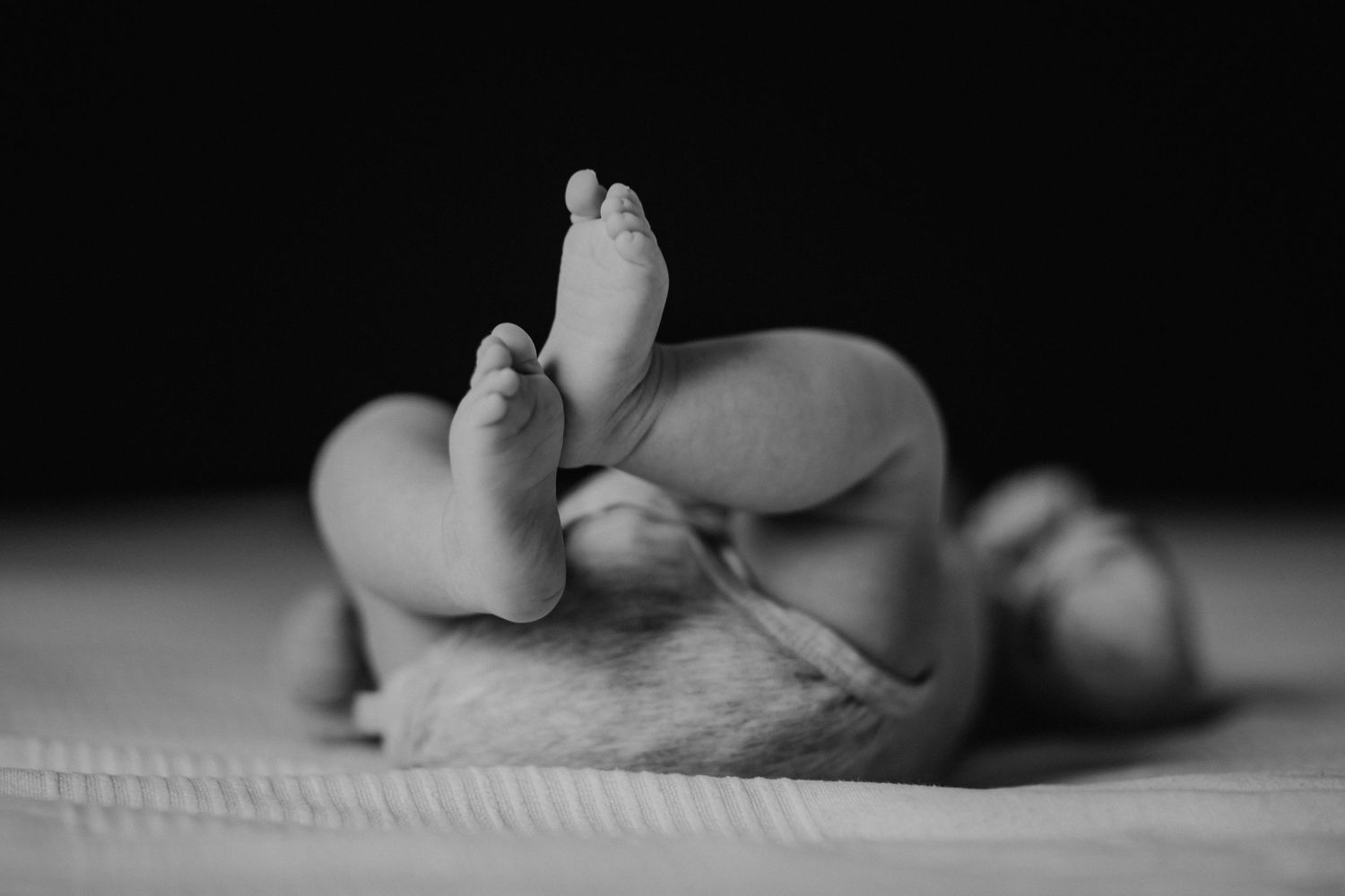 Nahaufnahme eines Schwarz-Weiß-Fotos von winzigen Babyfüßen vor einer strukturierten Decke.